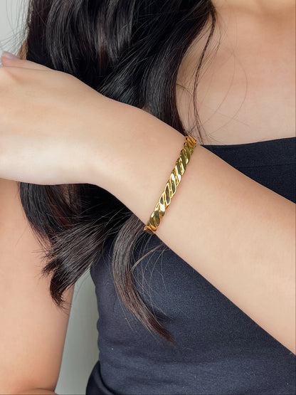A model wearing the Mila 18k gold PVD twisted cuff bangle with her forearm resting diagonally while gently touching her dark hair