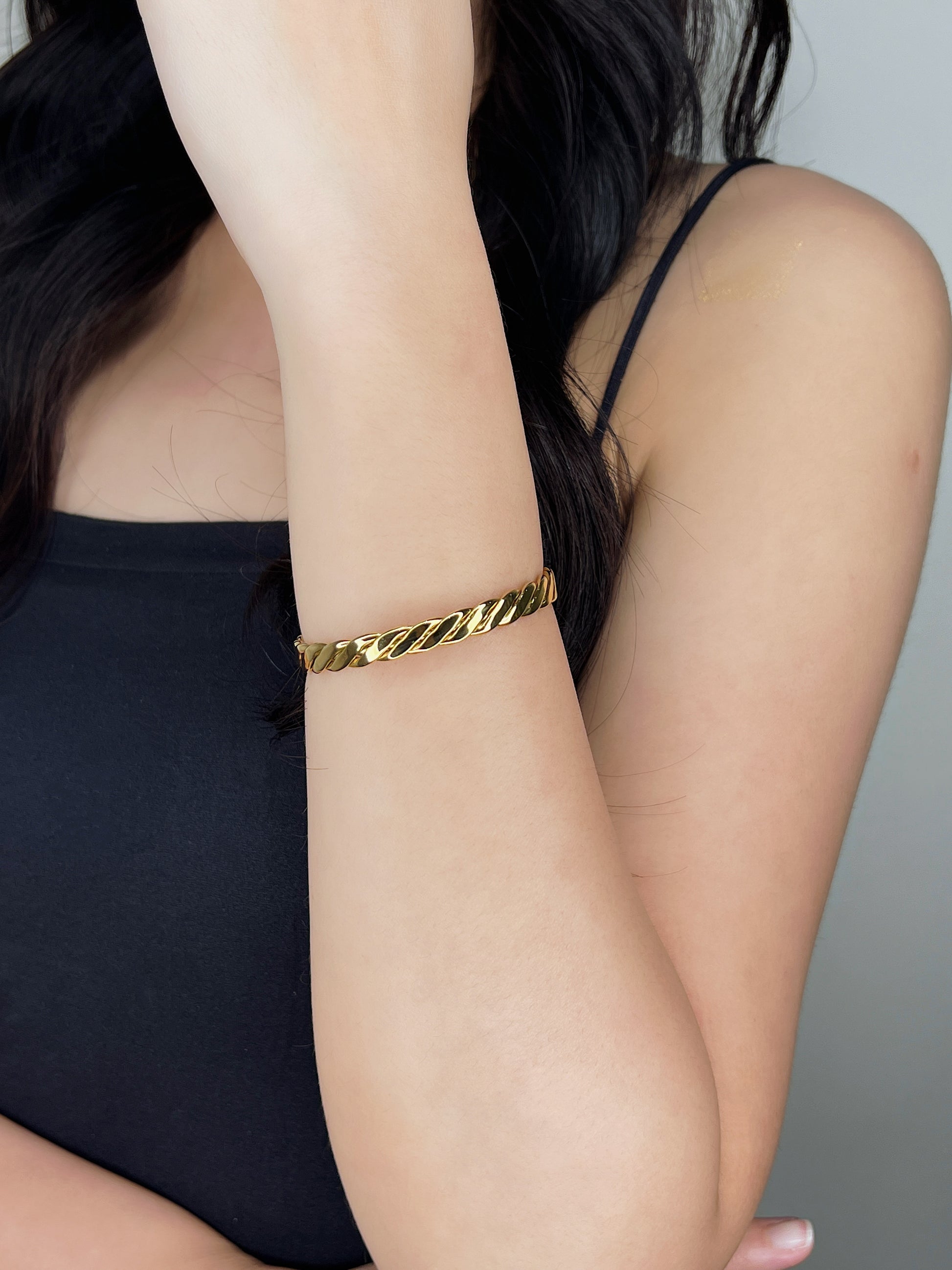 Close-up on-model view of the Mila gold braided cuff bangle shining on a wrist with the forearm held vertically against a black tube top