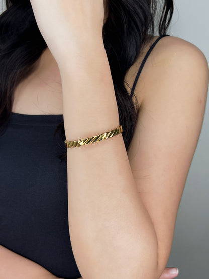 Close-up on-model view of the Mila gold braided cuff bangle shining on a wrist with the forearm held vertically against a black tube top
