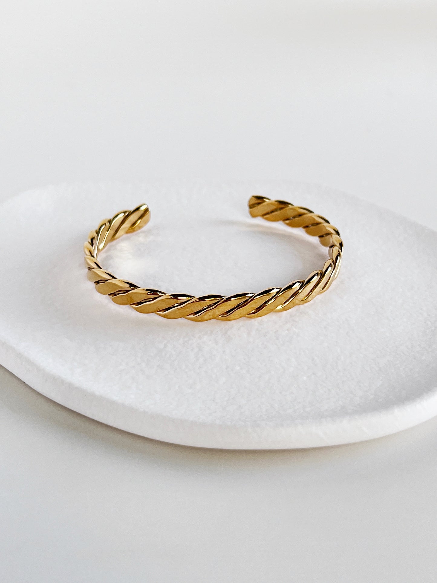 Balanced shot of the Mila gold braided open cuff bangle centered on a modern matte white porcelain plate, illustrating the symmetry of the braid