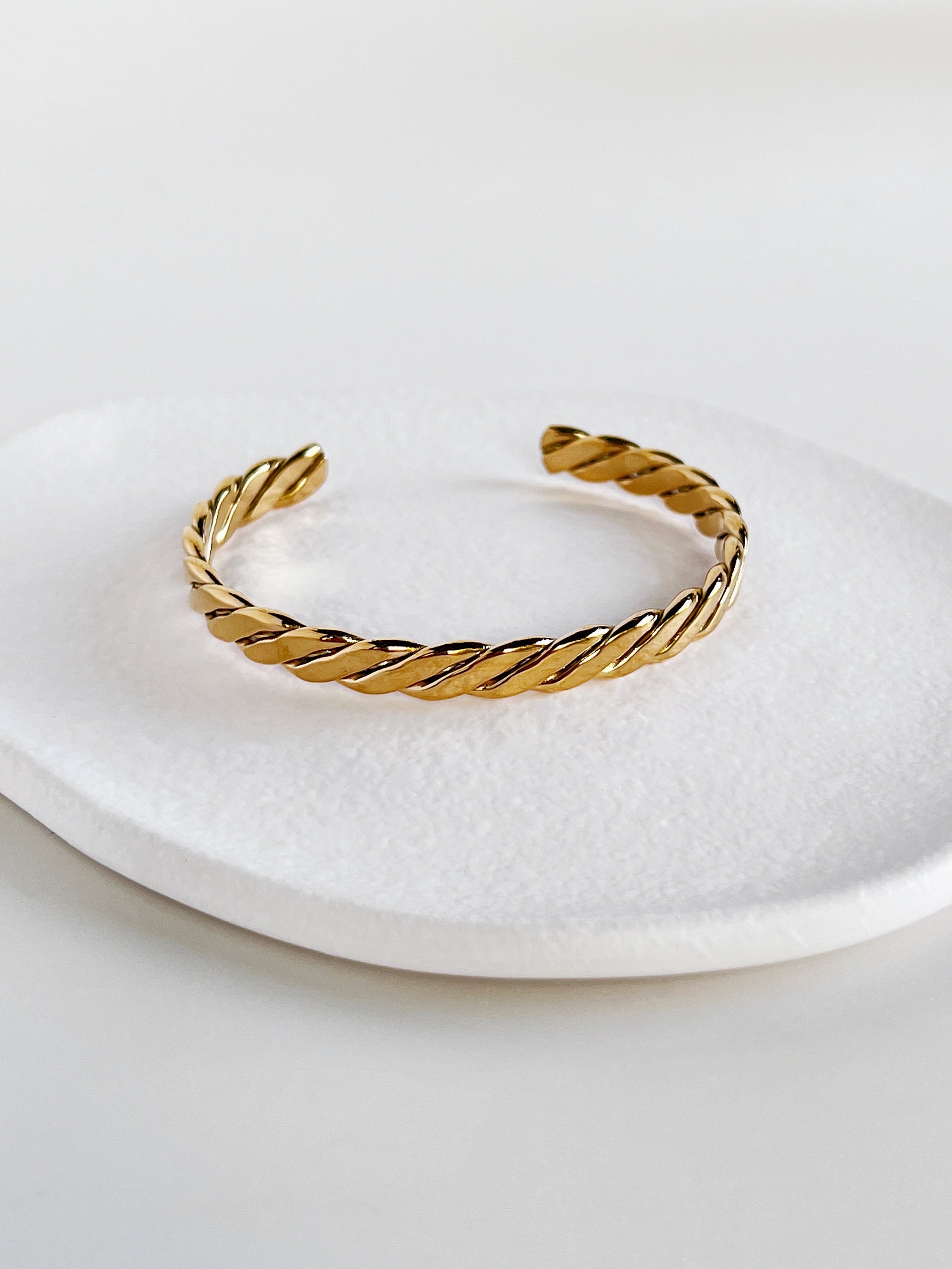 Balanced shot of the Mila gold braided open cuff bangle centered on a modern matte white porcelain plate, illustrating the symmetry of the braid