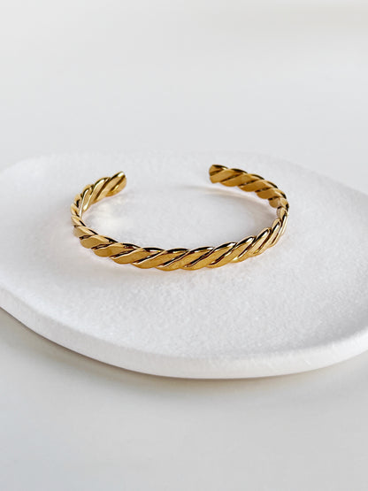 Balanced shot of the Mila gold braided open cuff bangle centered on a modern matte white porcelain plate, illustrating the symmetry of the braid