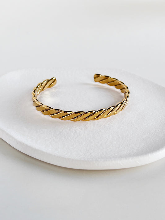 Balanced shot of the Mila gold braided open cuff bangle centered on a modern matte white porcelain plate, illustrating the symmetry of the braid