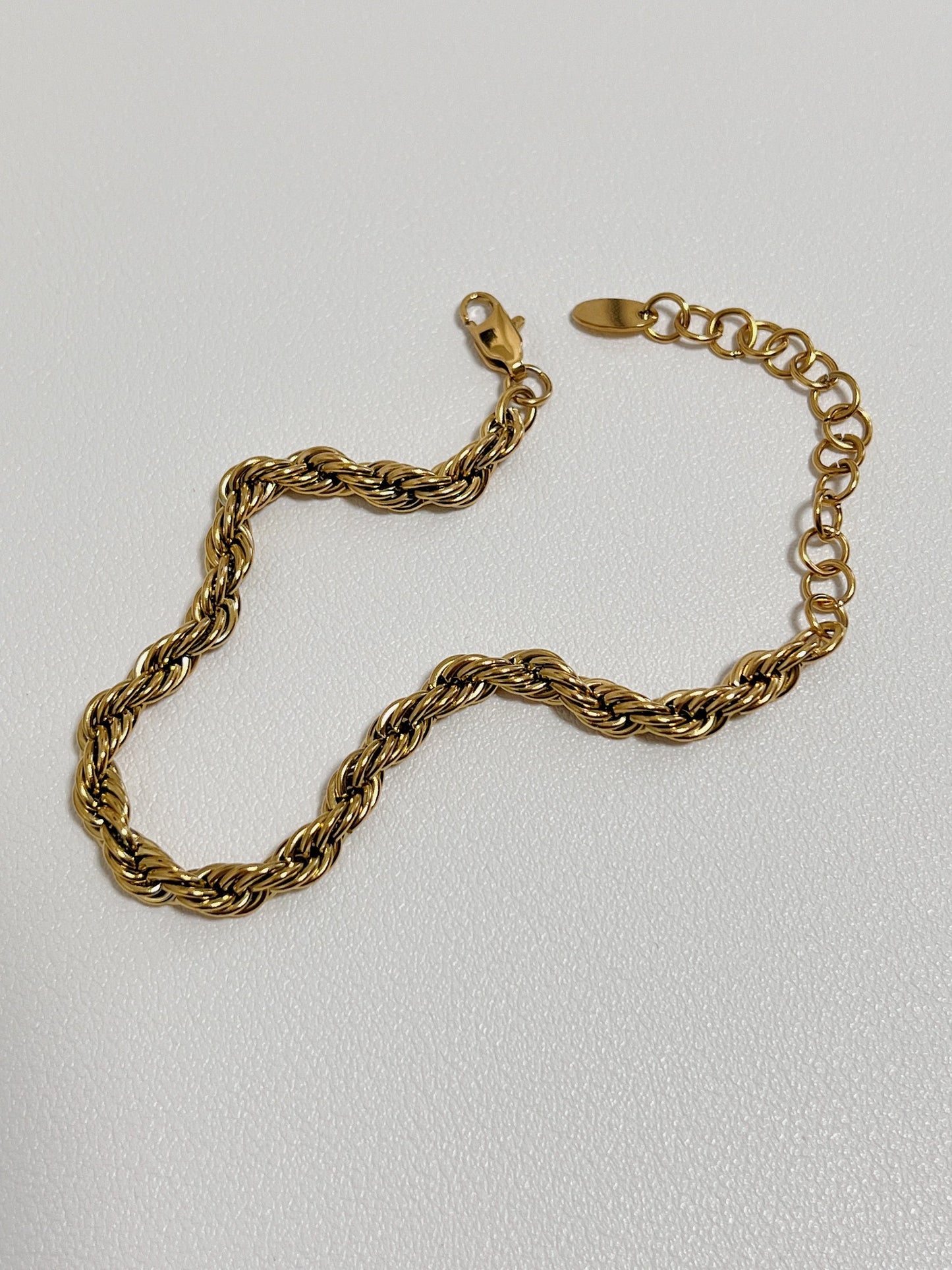 An editorial studio product shot of the Cali 5mm gold rope chain bracelet resting against a neutral backdrop.