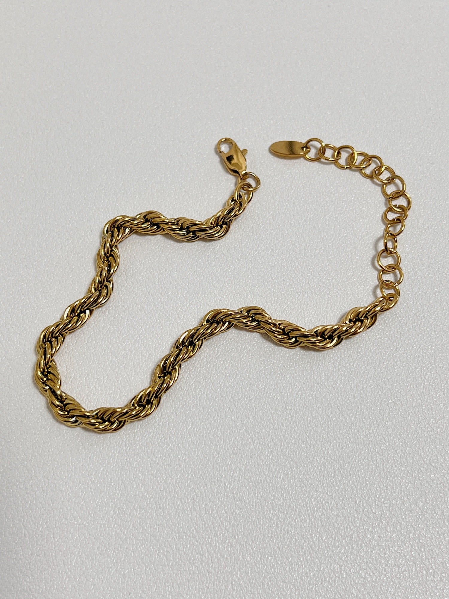 An editorial studio product shot of the Cali 5mm gold rope chain bracelet resting against a neutral backdrop.