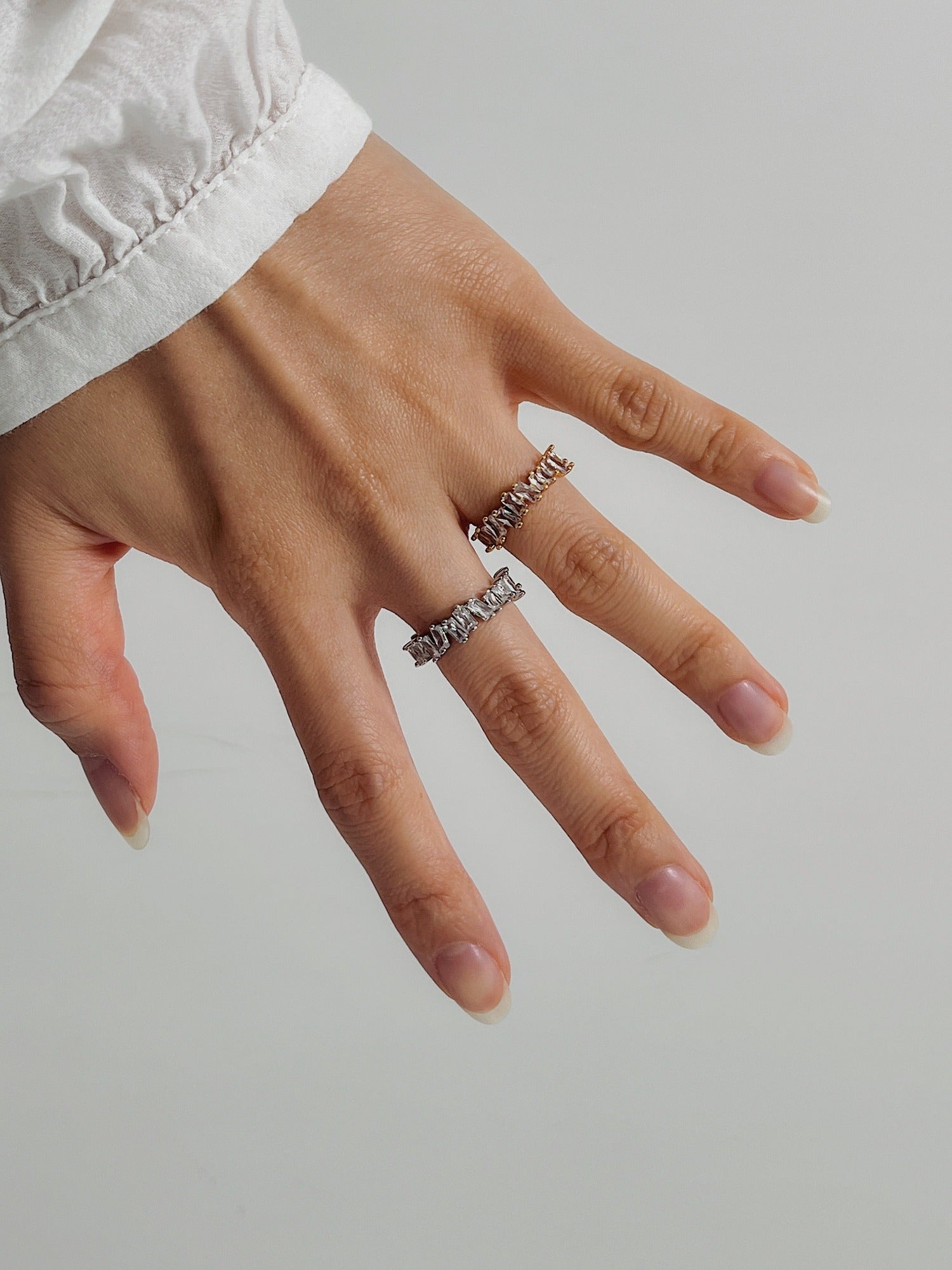 Hand stack featuring the Lizza eternity band in gold and silver tones with white blouse