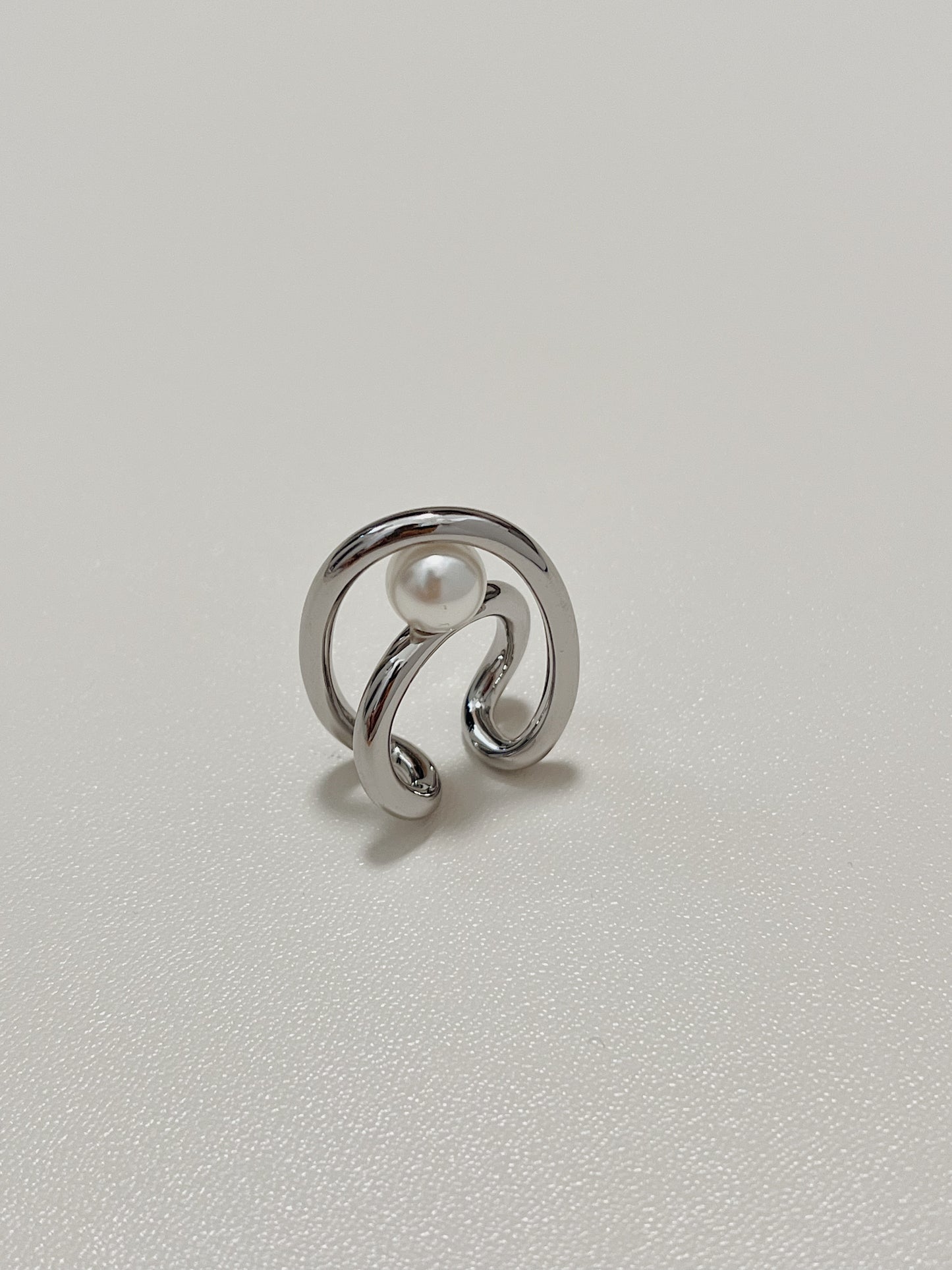 Isolated product view of the silver Karolina Statement Earlobe Cuff, showing how the open, non-adjustable double loop structure cradles the floating central pearl.