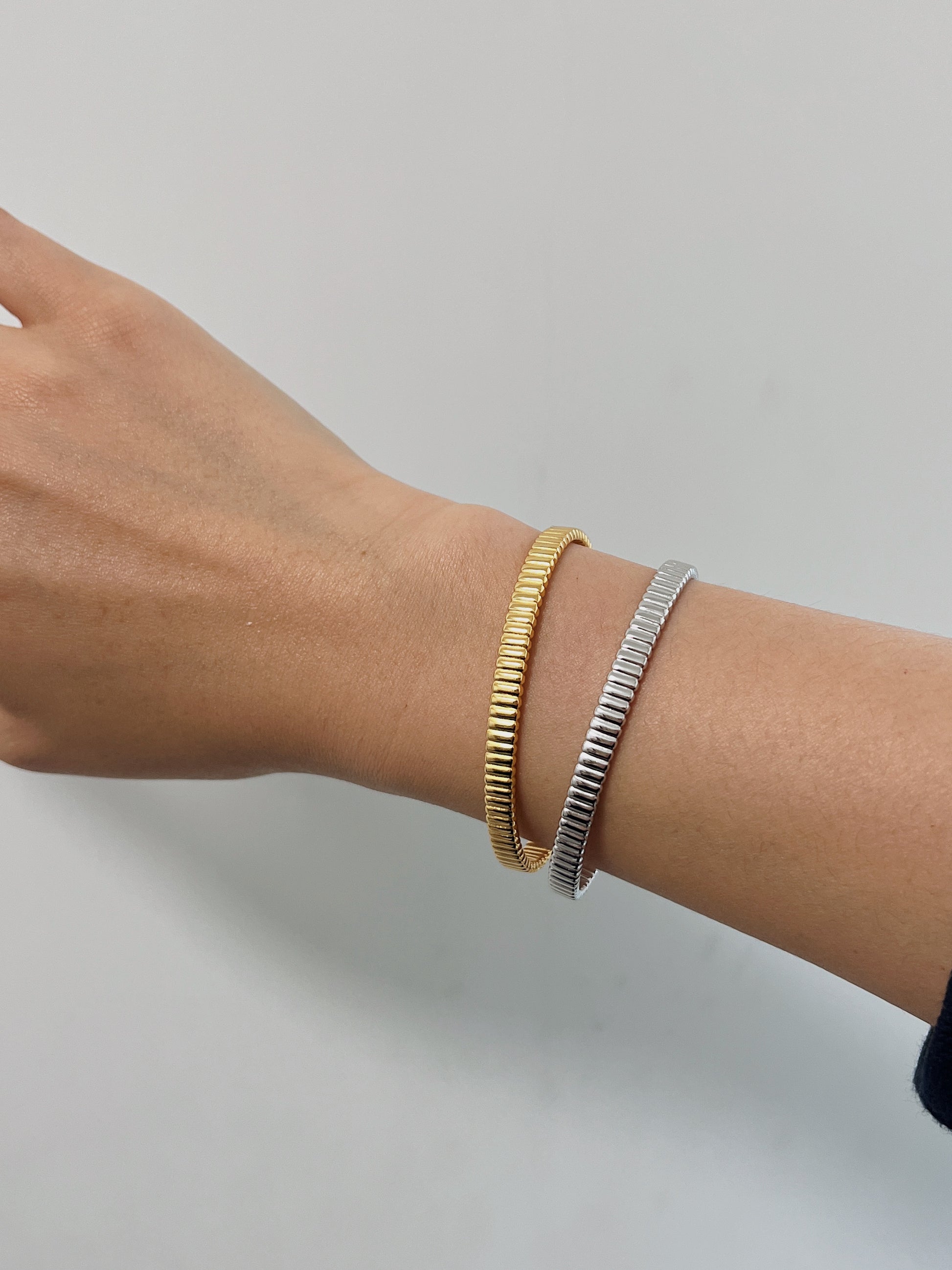 Detailed view of a model's arm displaying modern minimalist bracelet layering using two texturized open cuffs.