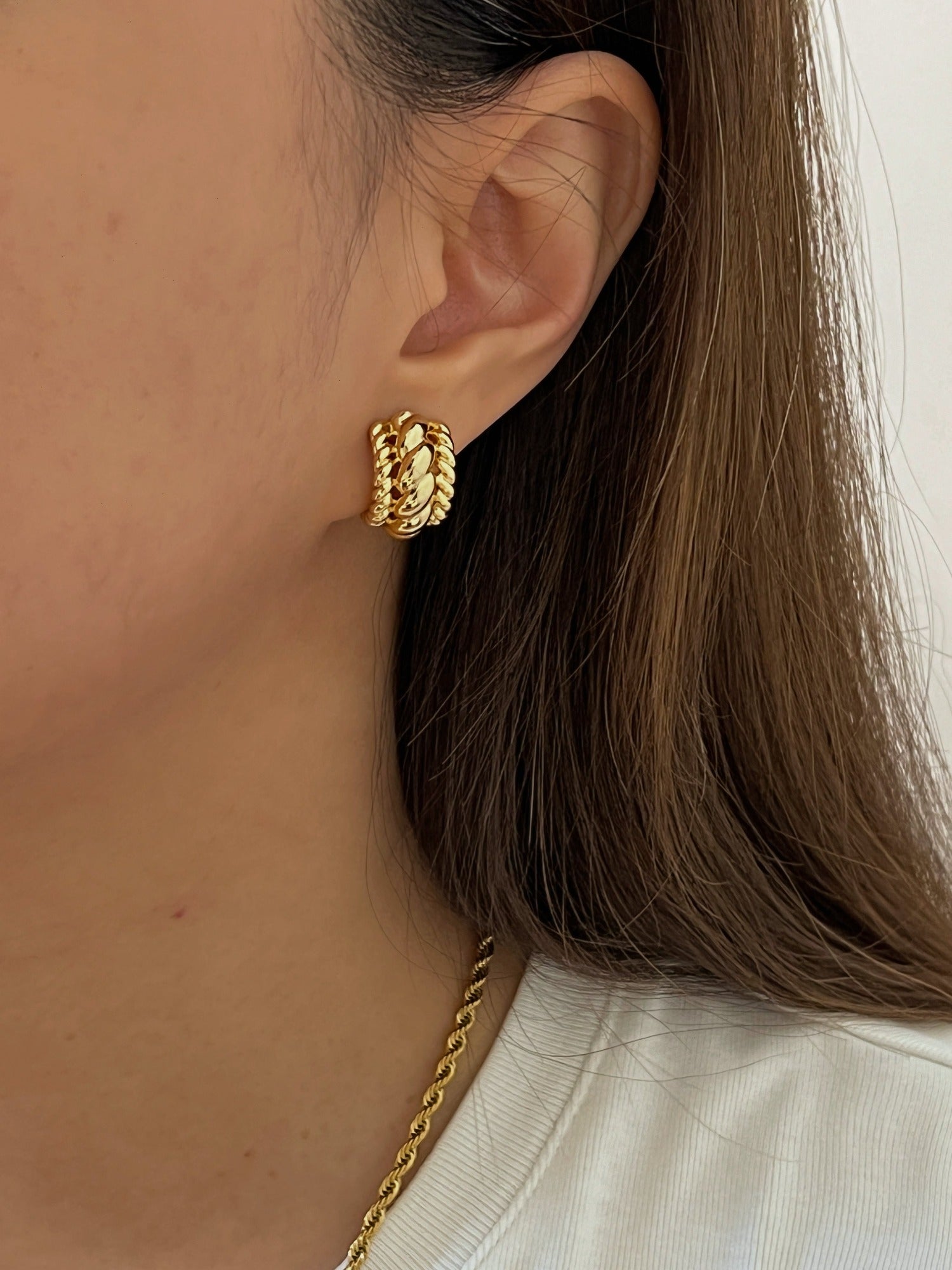 Lifestyle shot of a model styling gold rope earrings with a plain white shirt.