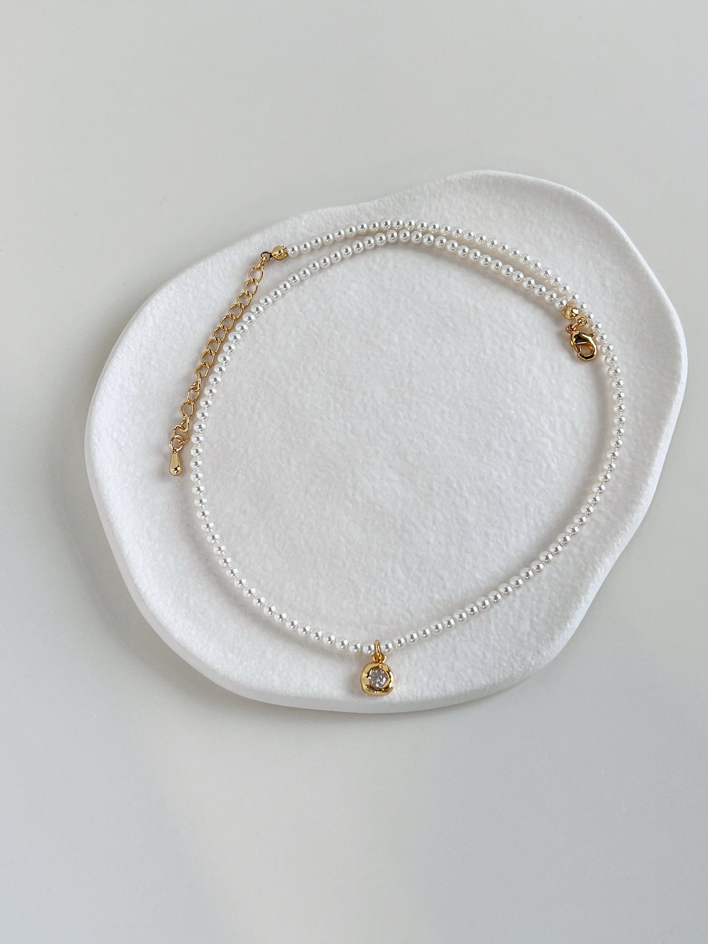Minimalist flatlay presentation showcasing the Alta pearl pendant strand on a ceramic plate