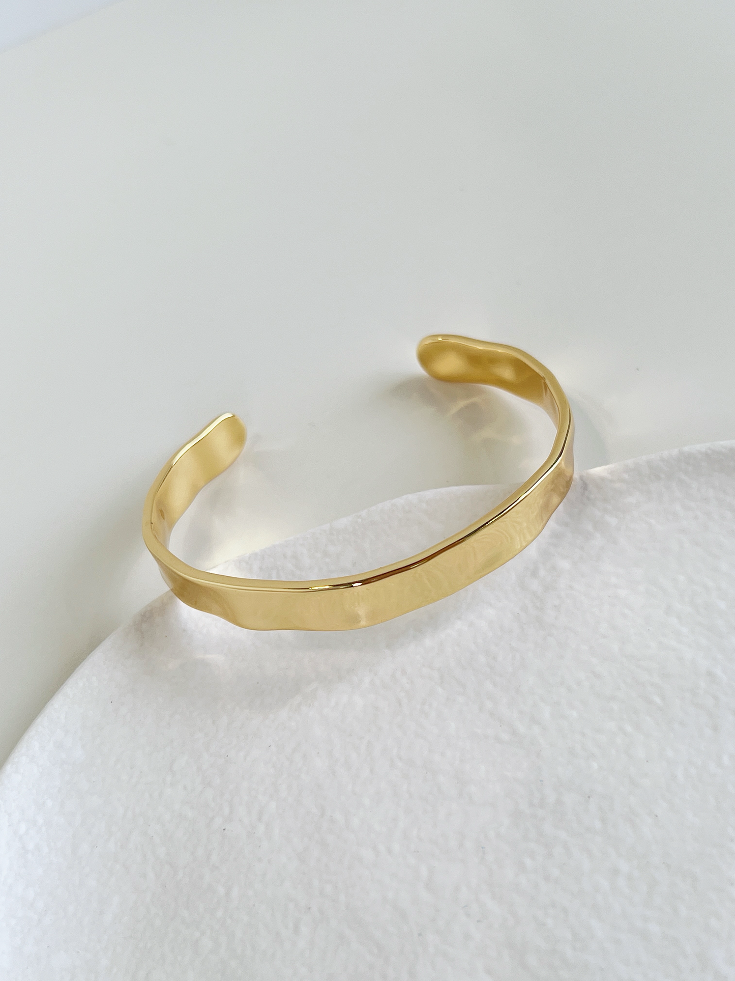 Top-down view of the Ella minimalist gold open cuff bangle resting on an organic-shaped white ceramic dish.