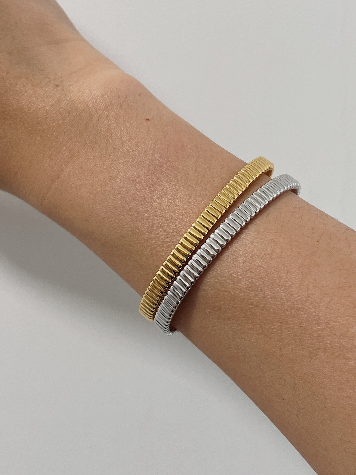 Model's wrist styled with a mixed-metal stack featuring both the 18K gold vermeil and sterling silver ribbed flexi cuff bangles against a clean background.