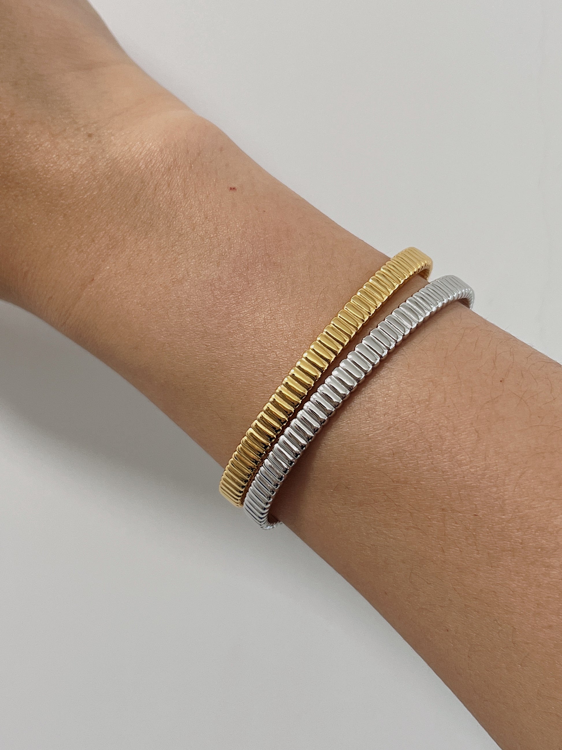Model's wrist styled with a mixed-metal stack featuring both the 18K gold vermeil and sterling silver ribbed flexi cuff bangles against a clean background.