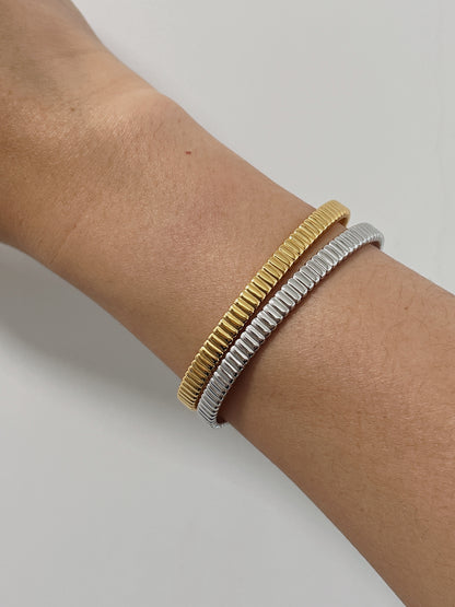 Model's wrist styled with a mixed-metal stack featuring both the 18K gold vermeil and sterling silver ribbed flexi cuff bangles against a clean background.