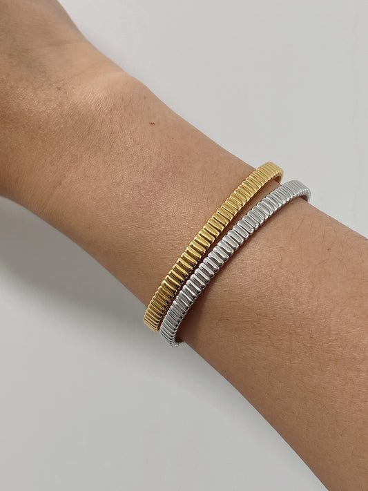 Model's wrist styled with a mixed-metal stack featuring both the 18K gold vermeil and sterling silver ribbed flexi cuff bangles against a clean background.