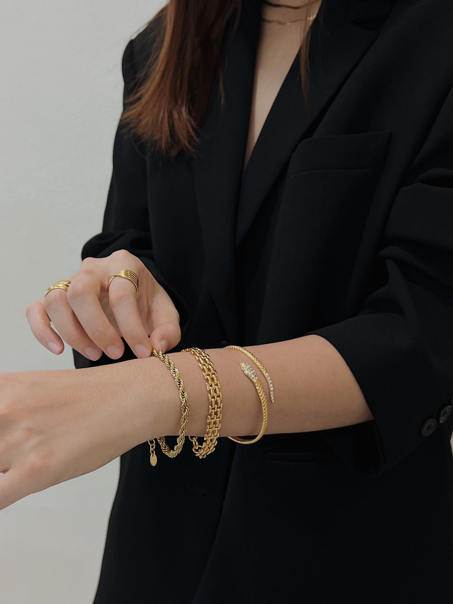 A model in a tailored black blazer adjusting her wrist stack featuring the Cali 5mm gold rope chain.