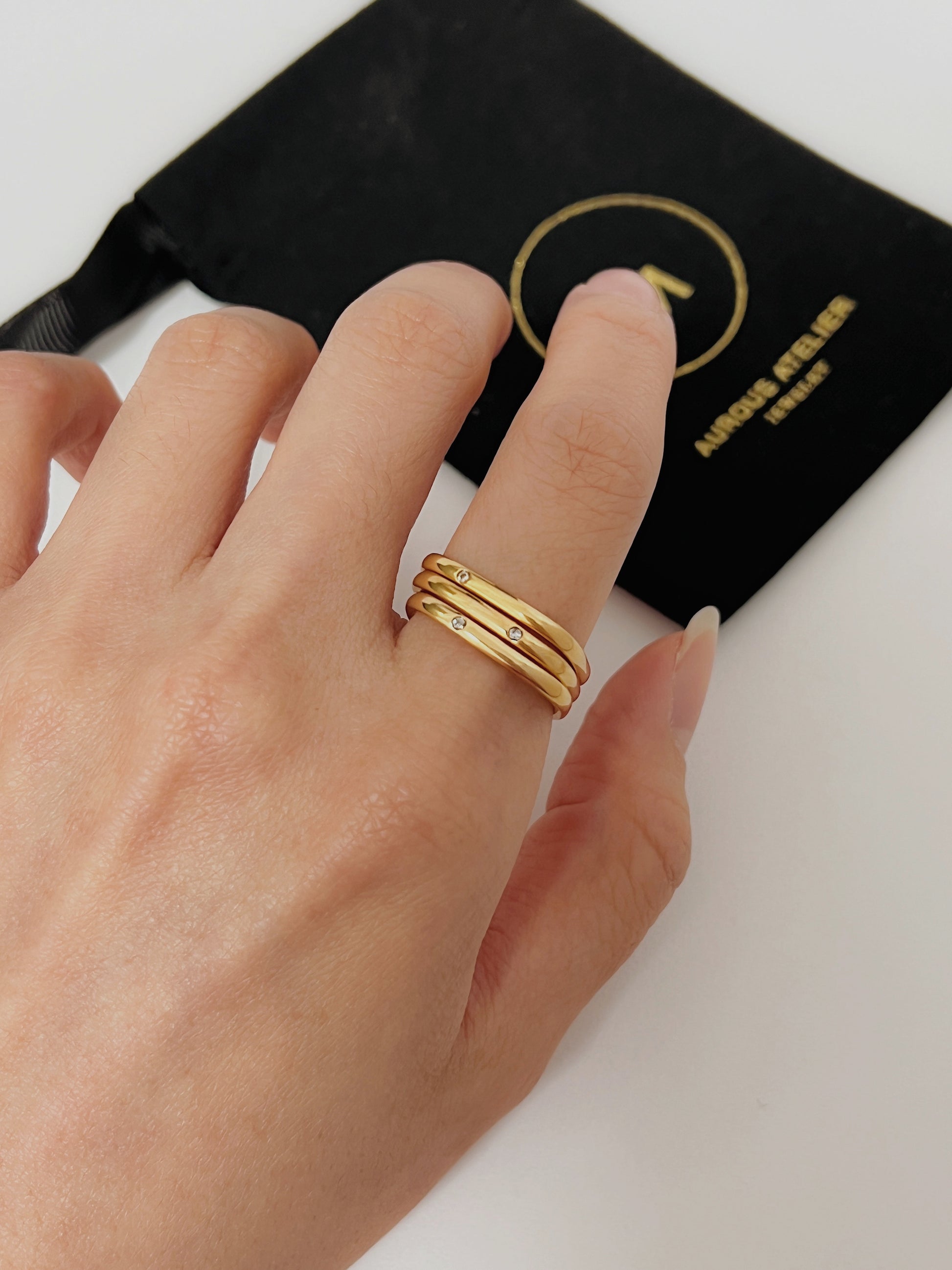Womens hand wearing the bold textural gold square ring resting beside Aurous  Atelier Branding Jewelry pouch