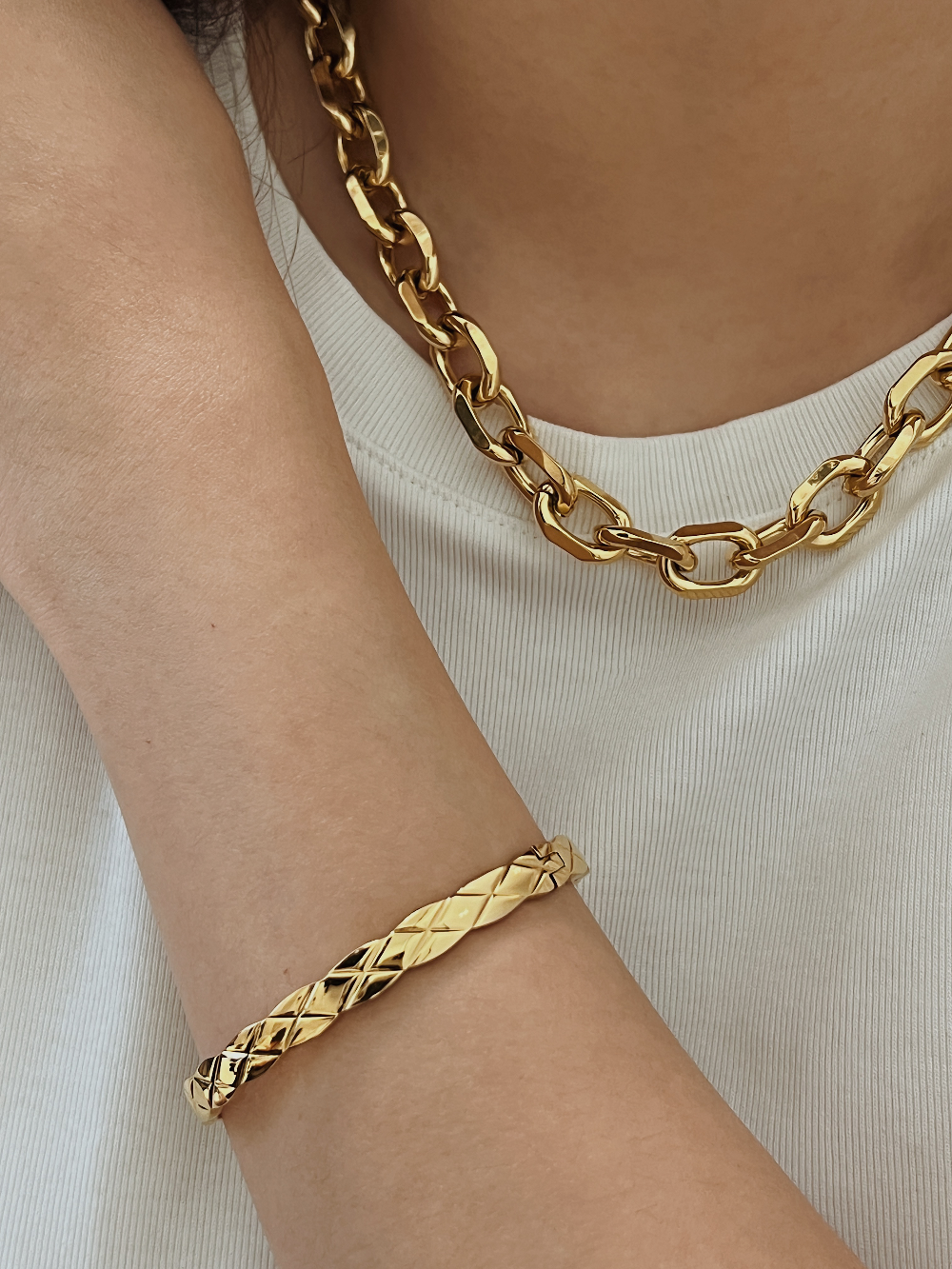 An elegant close-up of a model’s arm crossed over her chest, highlighting how the gold Corin quilted bangle catches light against a neutral fabric.