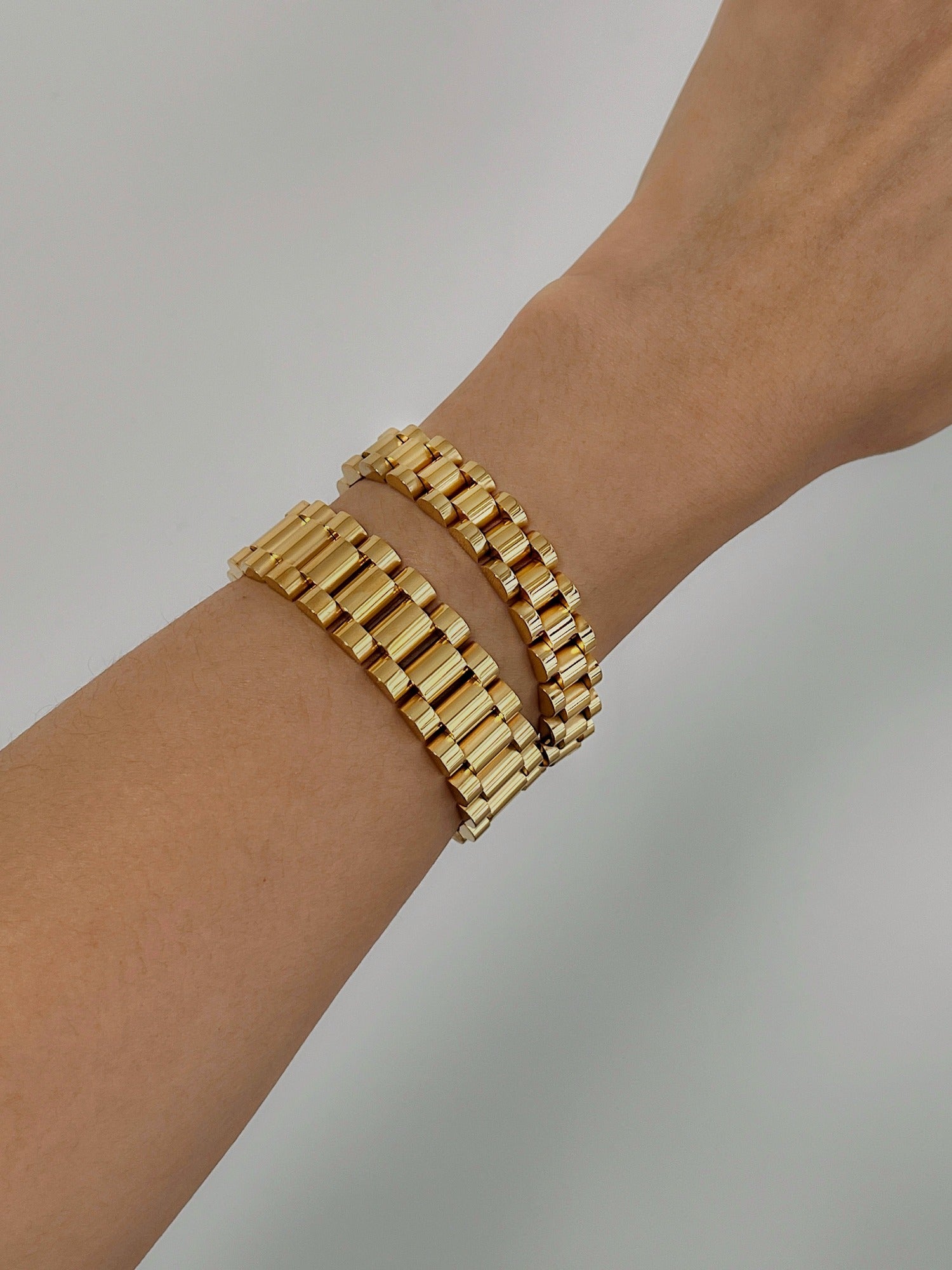Model showing both 10mm and 15mm gold watch link bracelets stacked together on arm.