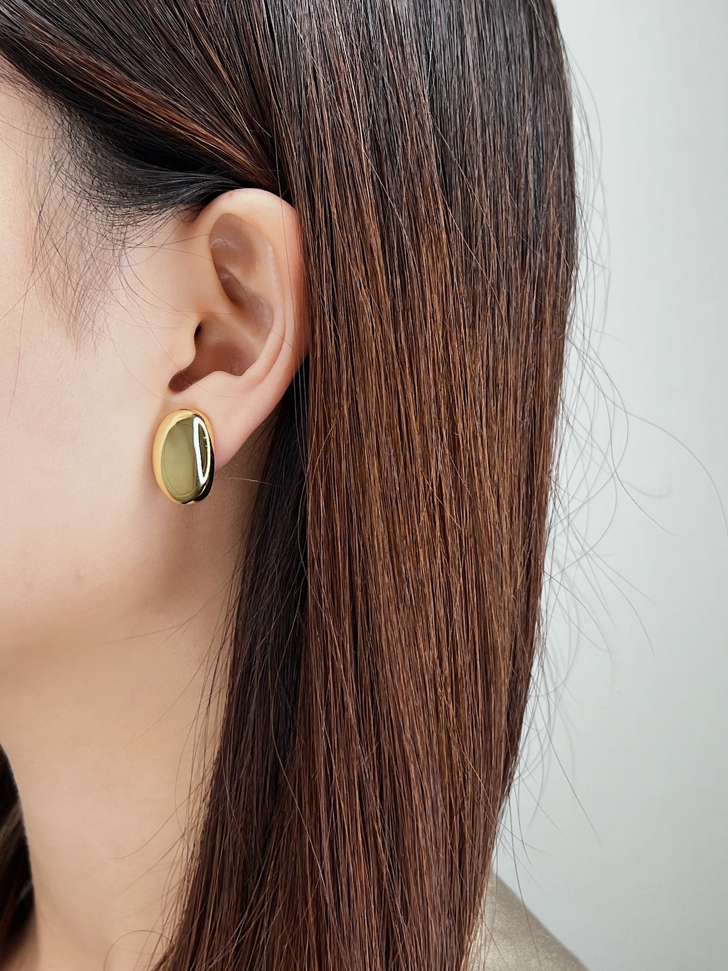 Model wearing the side-engraved gold oval clip on earrings paired with a neutral minimalist linen blazer.