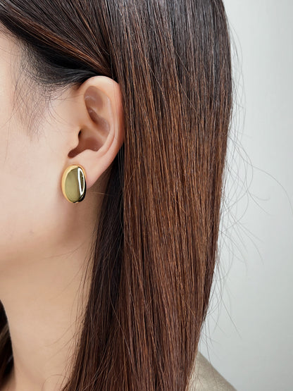 Model wearing the side-engraved gold oval clip on earrings paired with a neutral minimalist linen blazer.