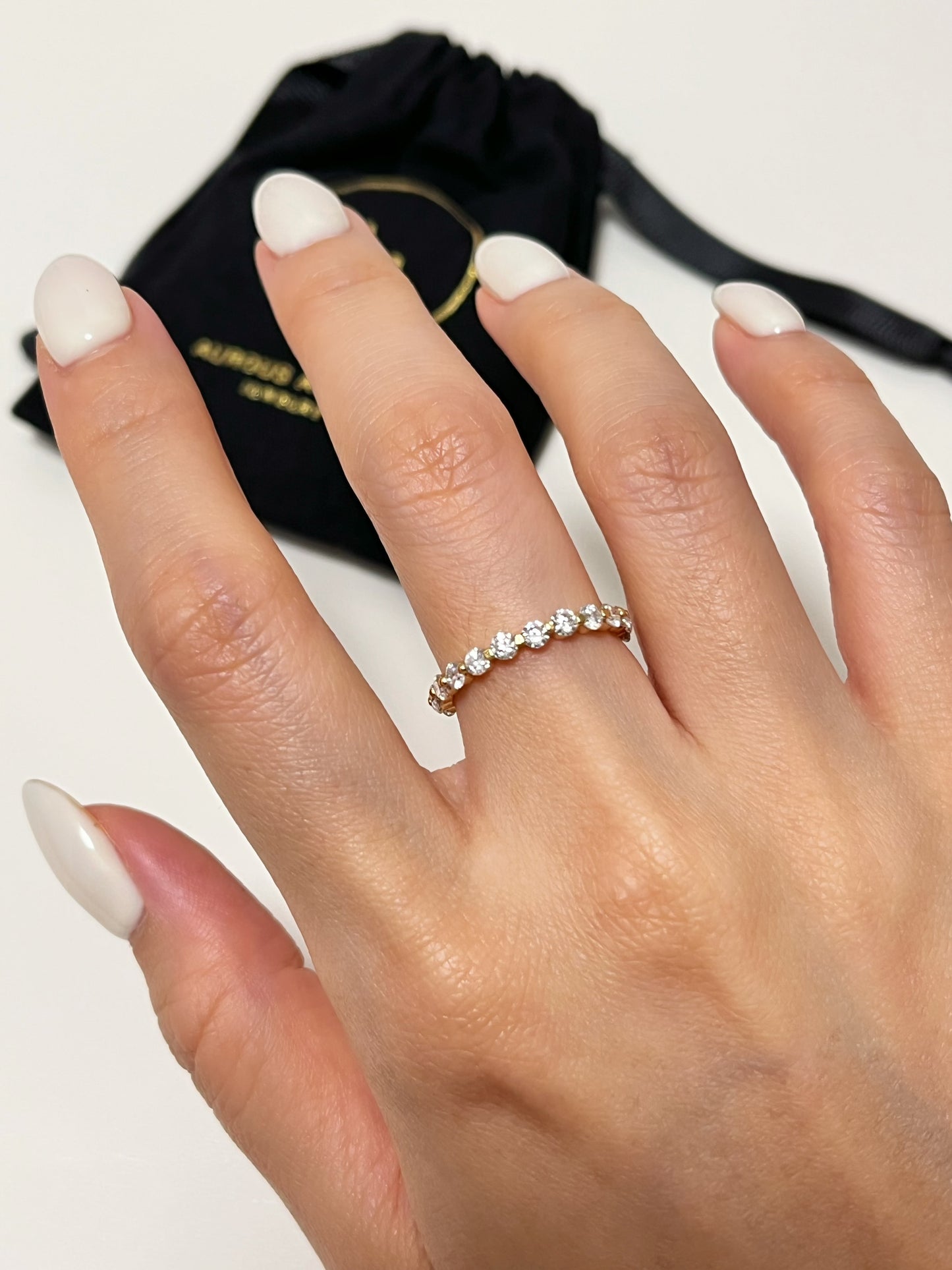Model modeling the Callie gold moissanite eternity ring on an middle finger against a blurred black jewelry pouch