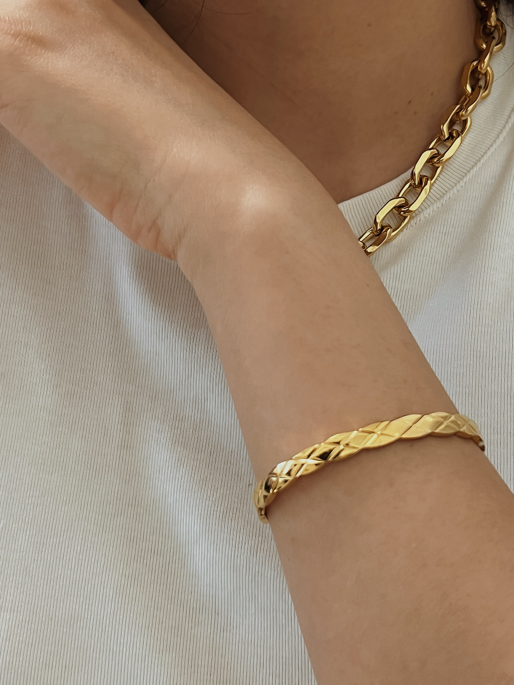 close-up of a model wearing the Corin gold quilted hinged bangle on her wrist, styled casually with a premium white ribbed top.