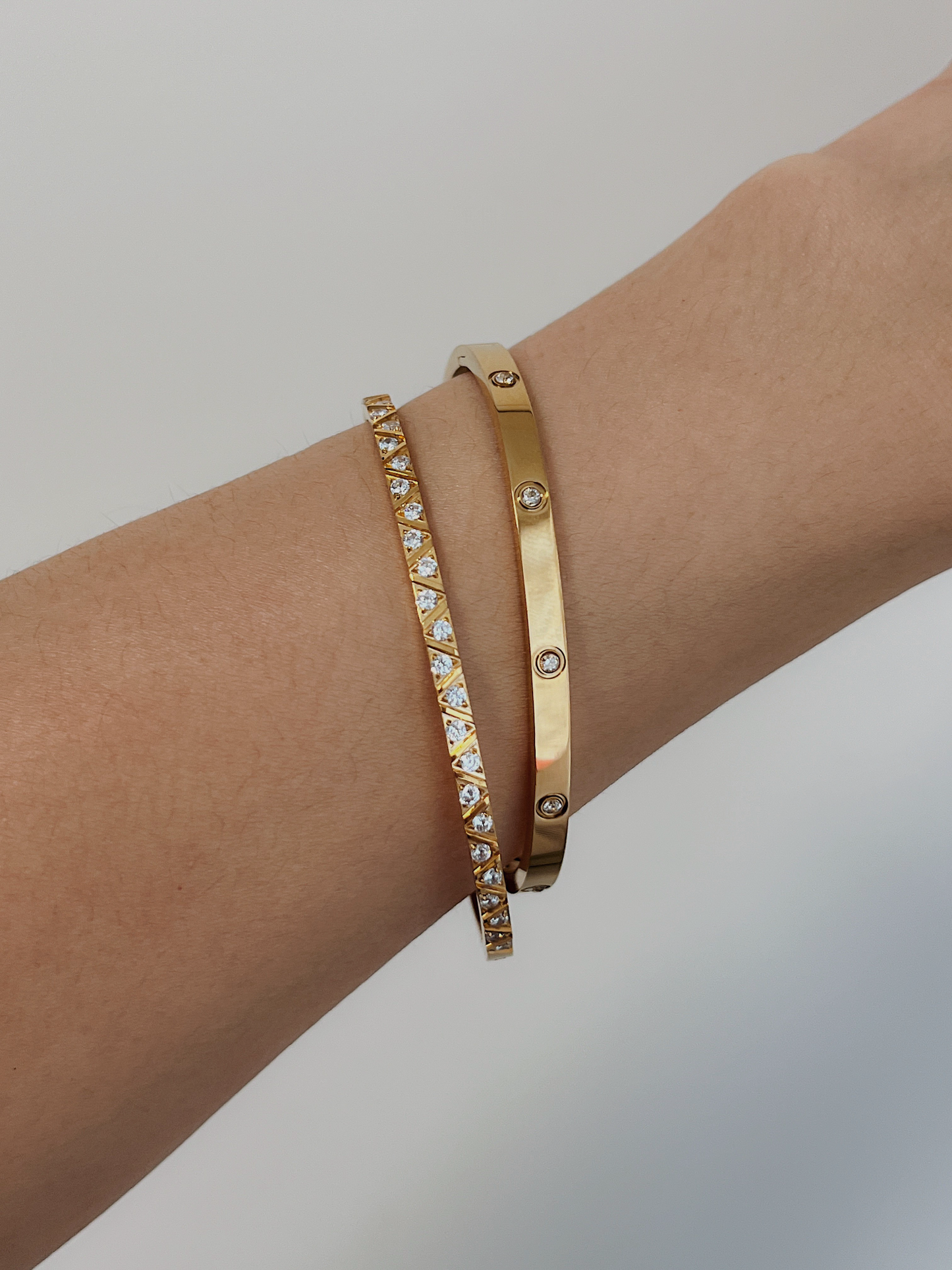 A model's arm styled with a stack of the Gia geometric gemstone bangle and the Dane bezel-set gold bangle against a clean, neutral backdrop.