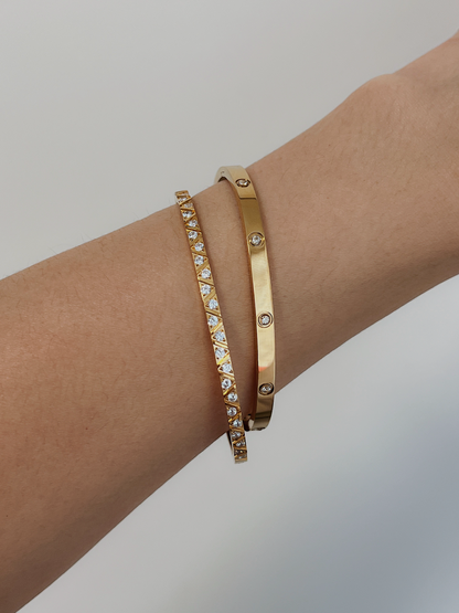A model's arm styled with a stack of the Gia geometric gemstone bangle and the Dane bezel-set gold bangle against a clean, neutral backdrop.