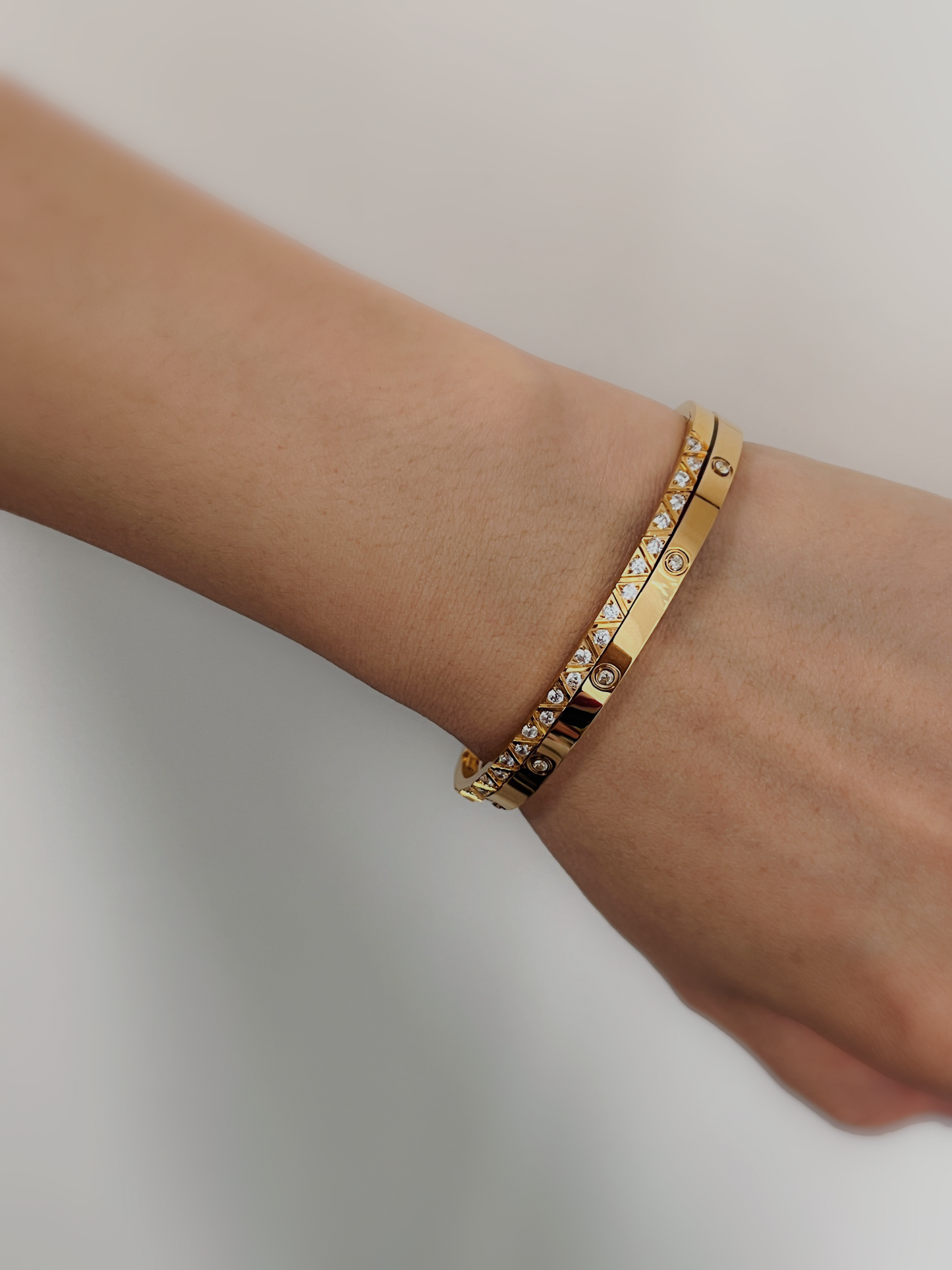 A close-up of a model's wrist wearing a stack of the Gia and Dane gold gemstone bangles, styled with a cozy neutral knit sleeve.