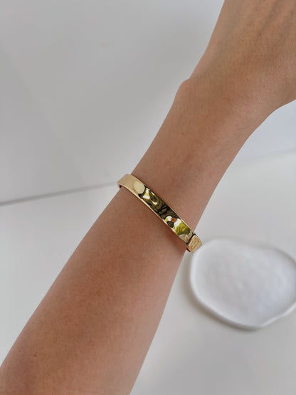 Close-up of a model wearing the Ella hammered gold cuff bangle on a bare wrist against a crisp white backdrop.