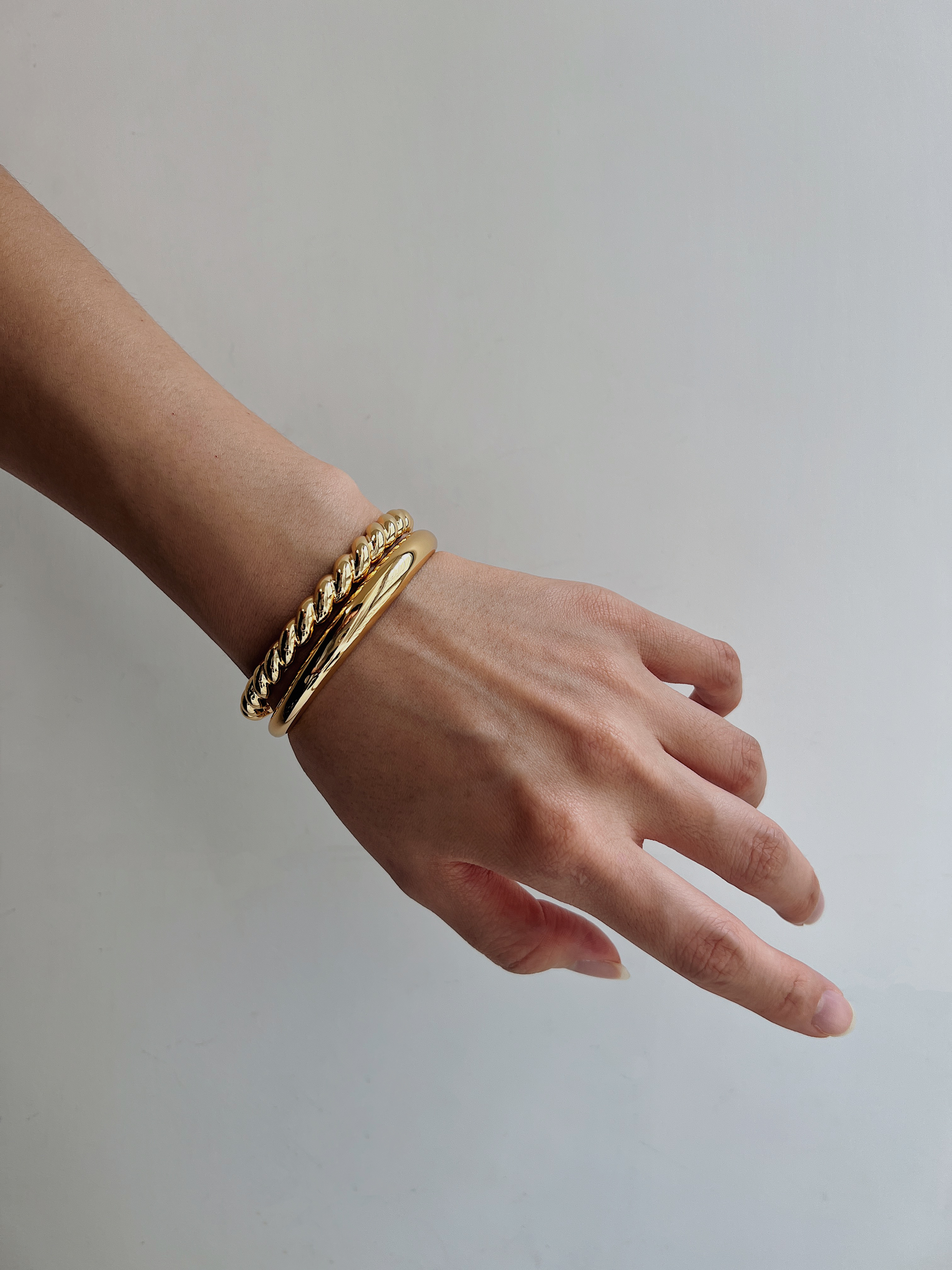 Close-up of a model's arm styling the Paris Croissant and London Plain gold cuff bracelets stacked together against a neutral backdrop.