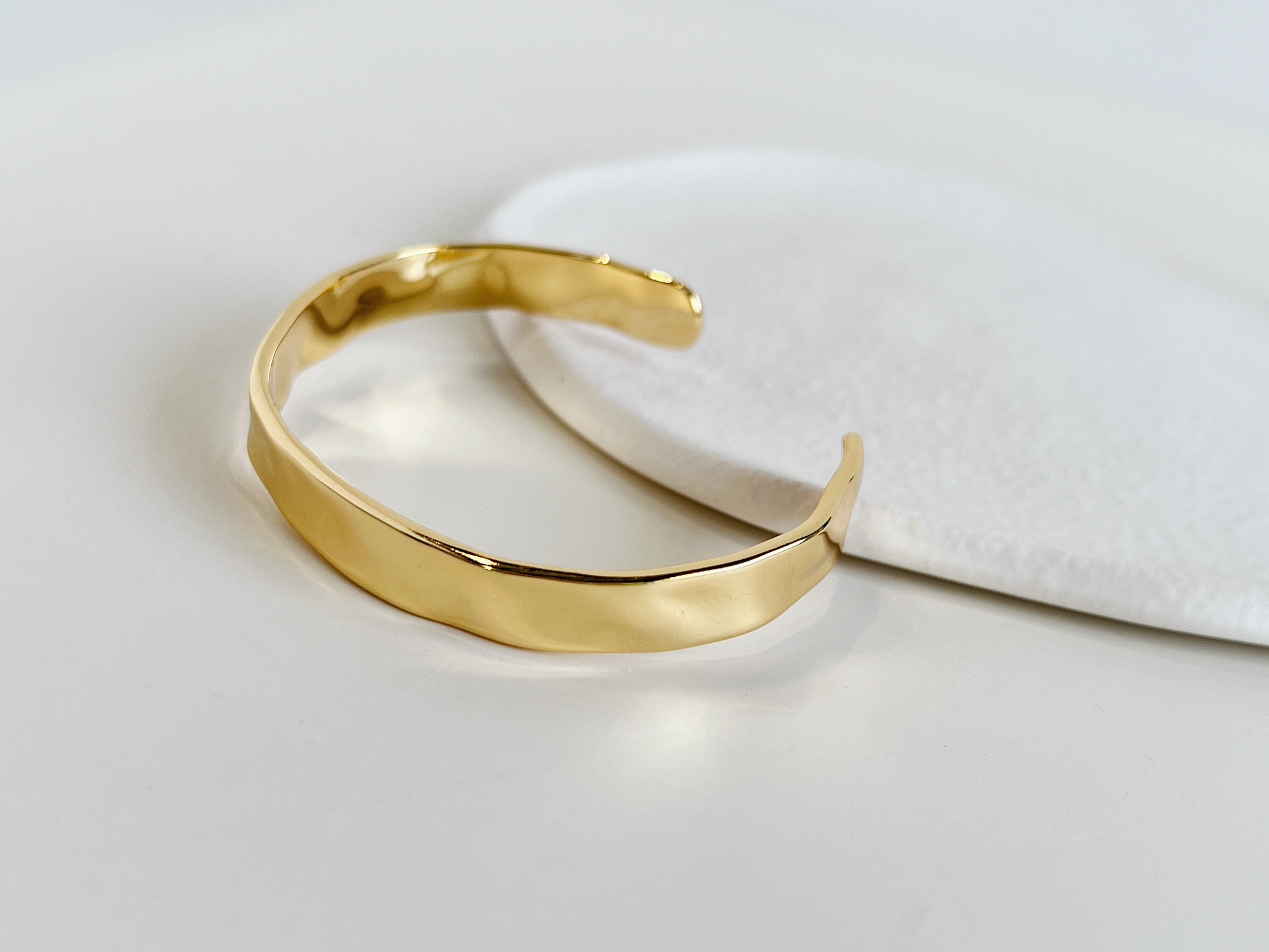 Still life studio imagery capturing the molten, liquid-like reflections on a textured gold cuff bracelet.