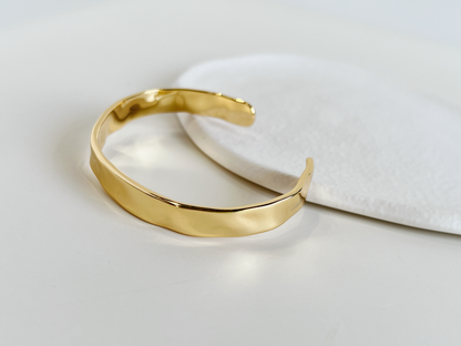 Still life studio imagery capturing the molten, liquid-like reflections on a textured gold cuff bracelet.