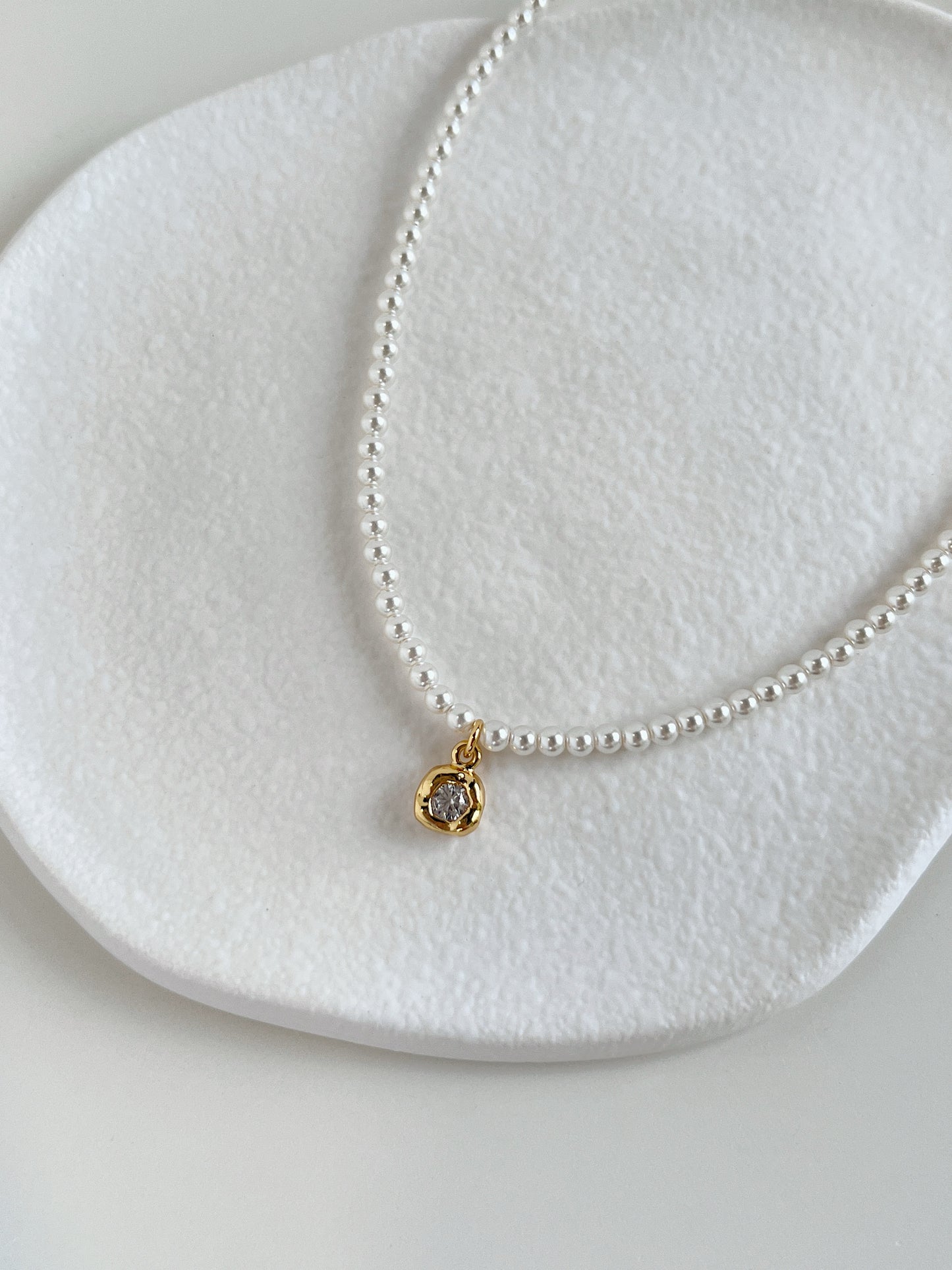 Close-up catalog shot highlighting the natural white luster of a premium dainty pearl chain resting against a neutral stone ledge