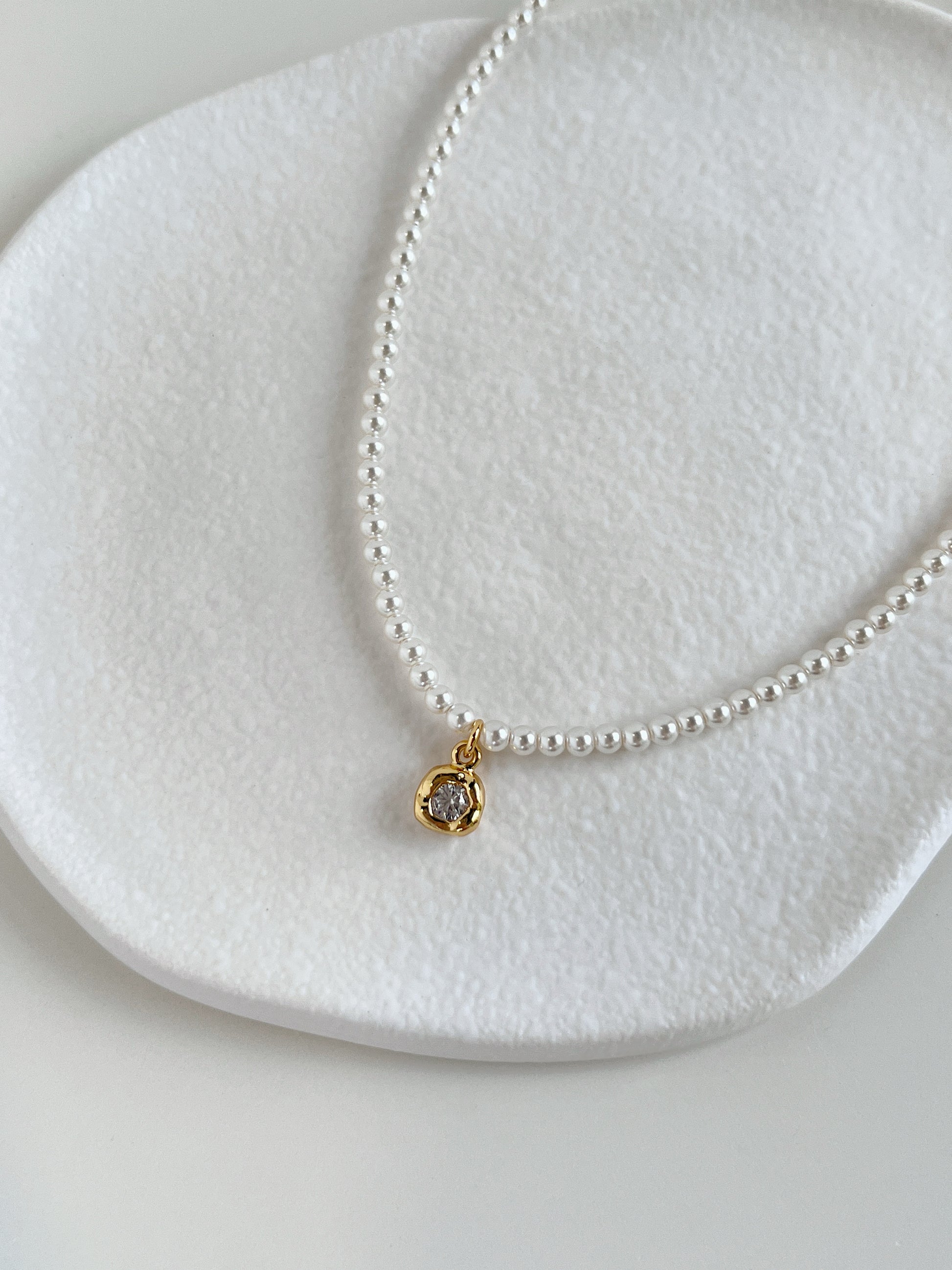 Close-up catalog shot highlighting the natural white luster of a premium dainty pearl chain resting against a neutral stone ledge