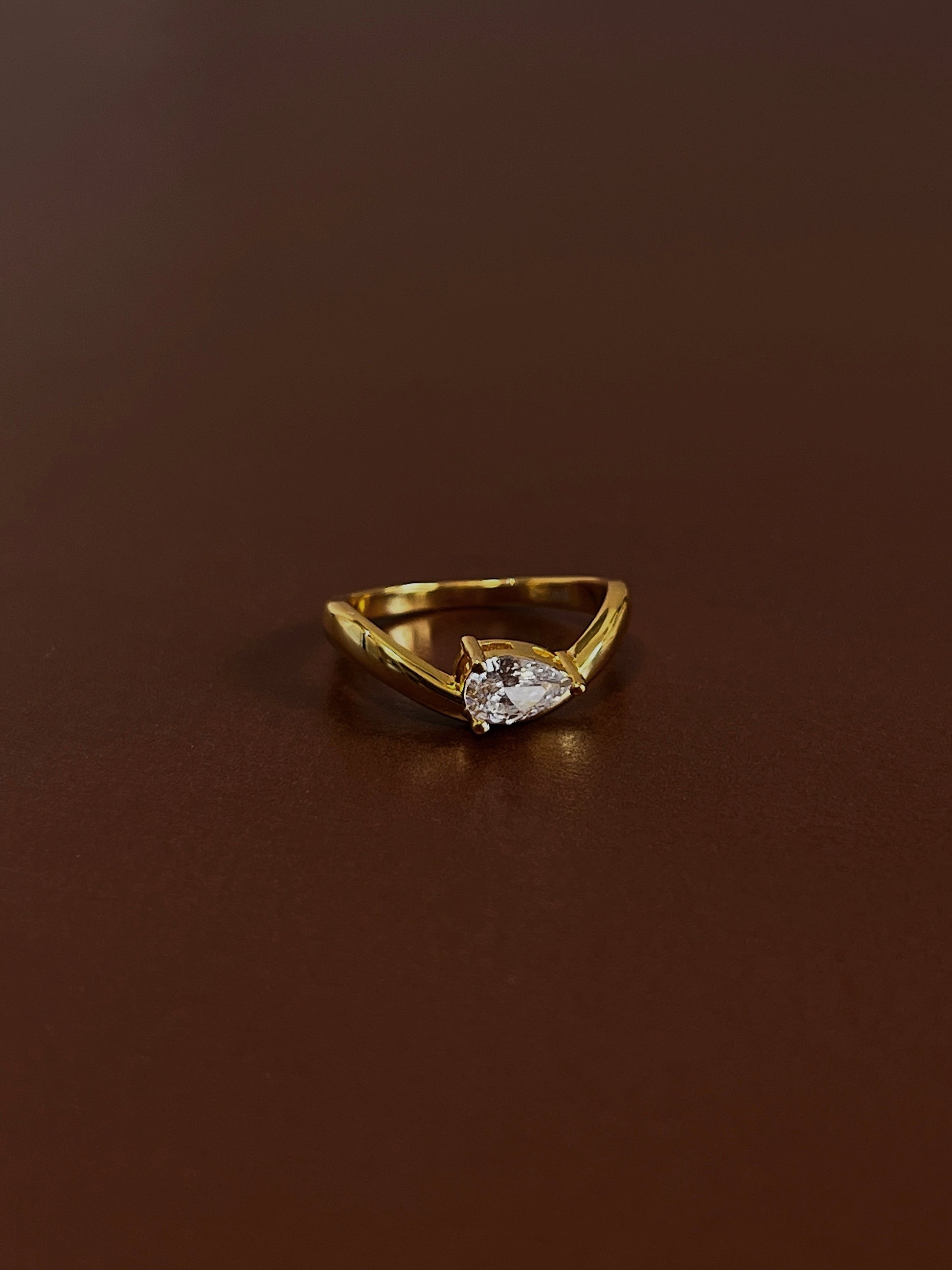 Nova pear solitaire wave ring in 18k gold vermeil with pear-cut moissanite stone on dark brown textured background