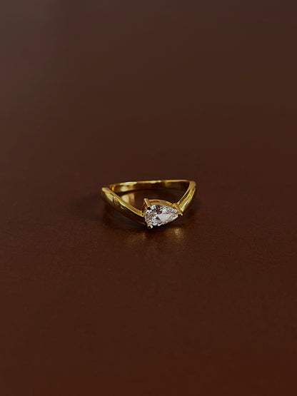 Nova pear solitaire wave ring in 18k gold vermeil with pear-cut moissanite stone on dark brown textured background