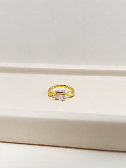 Nova pear cut moissanite solitaire wave pinky ring in 18k gold vermeil over s925 sterling silver resting on cream display pedestal