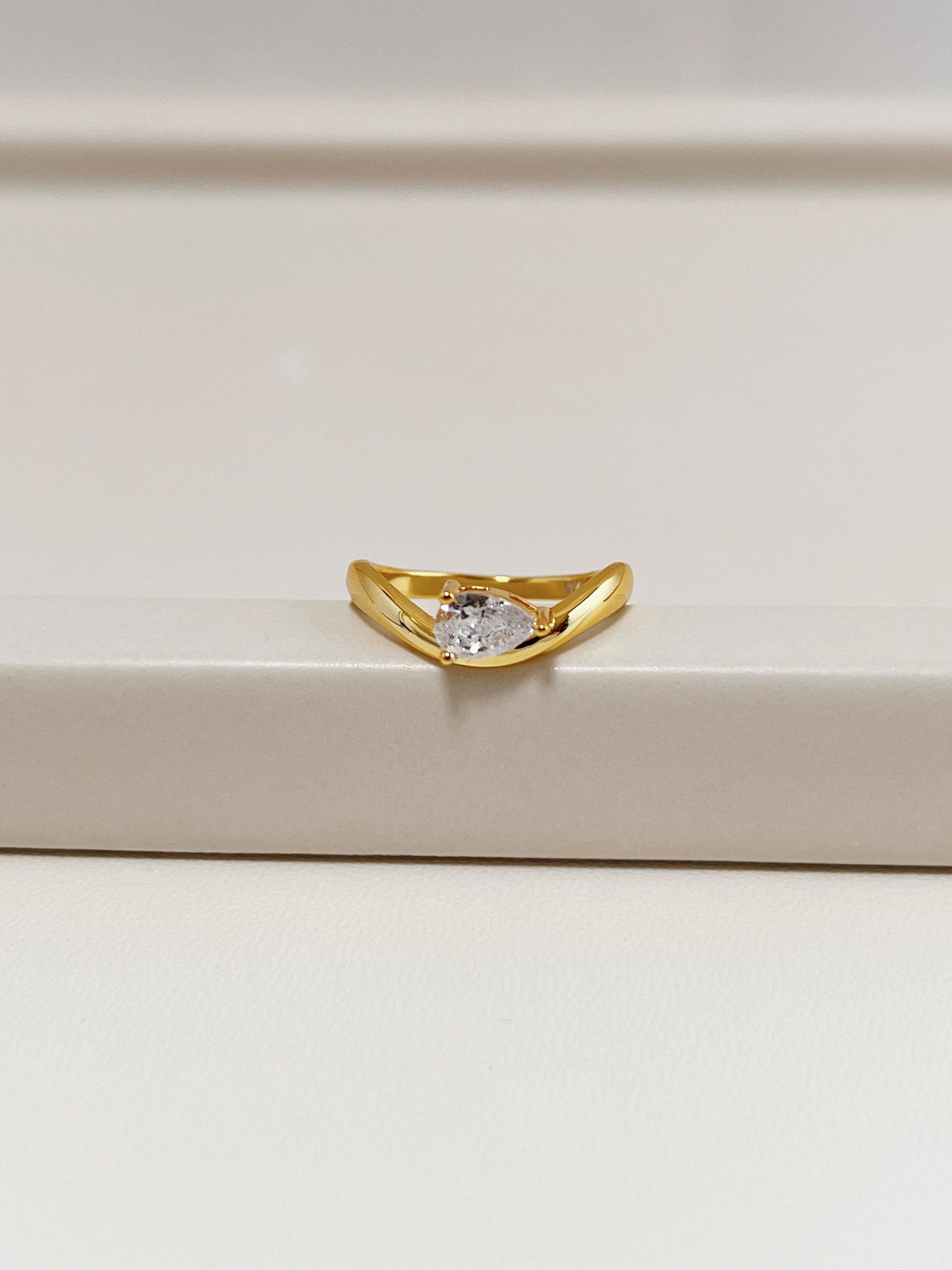 gold nova wave ring with pear moissanite resting on neutral tray