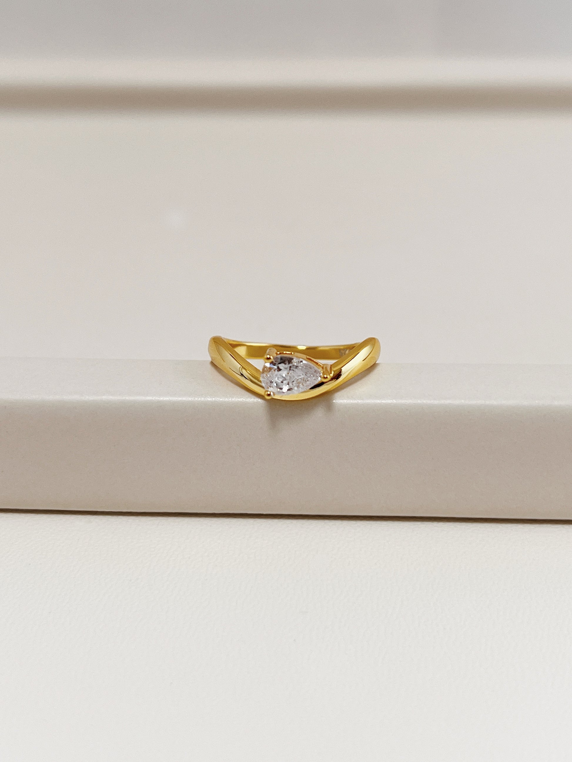 gold nova wave ring with pear moissanite resting on neutral tray