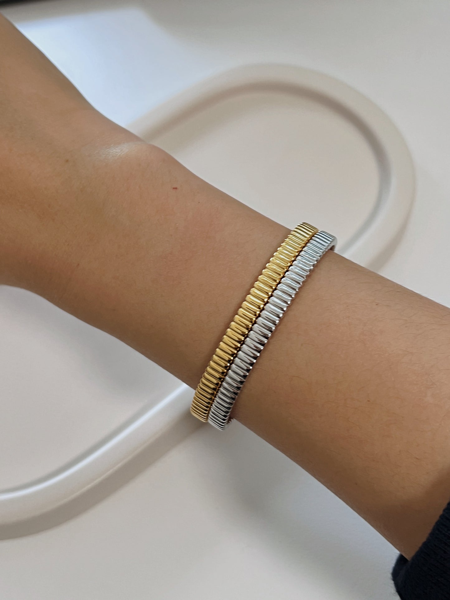Lifestyle portrait focusing on a model's arm adorned with stacked ribbed gold and silver bangles, capturing a casual yet high-end luxury feel.