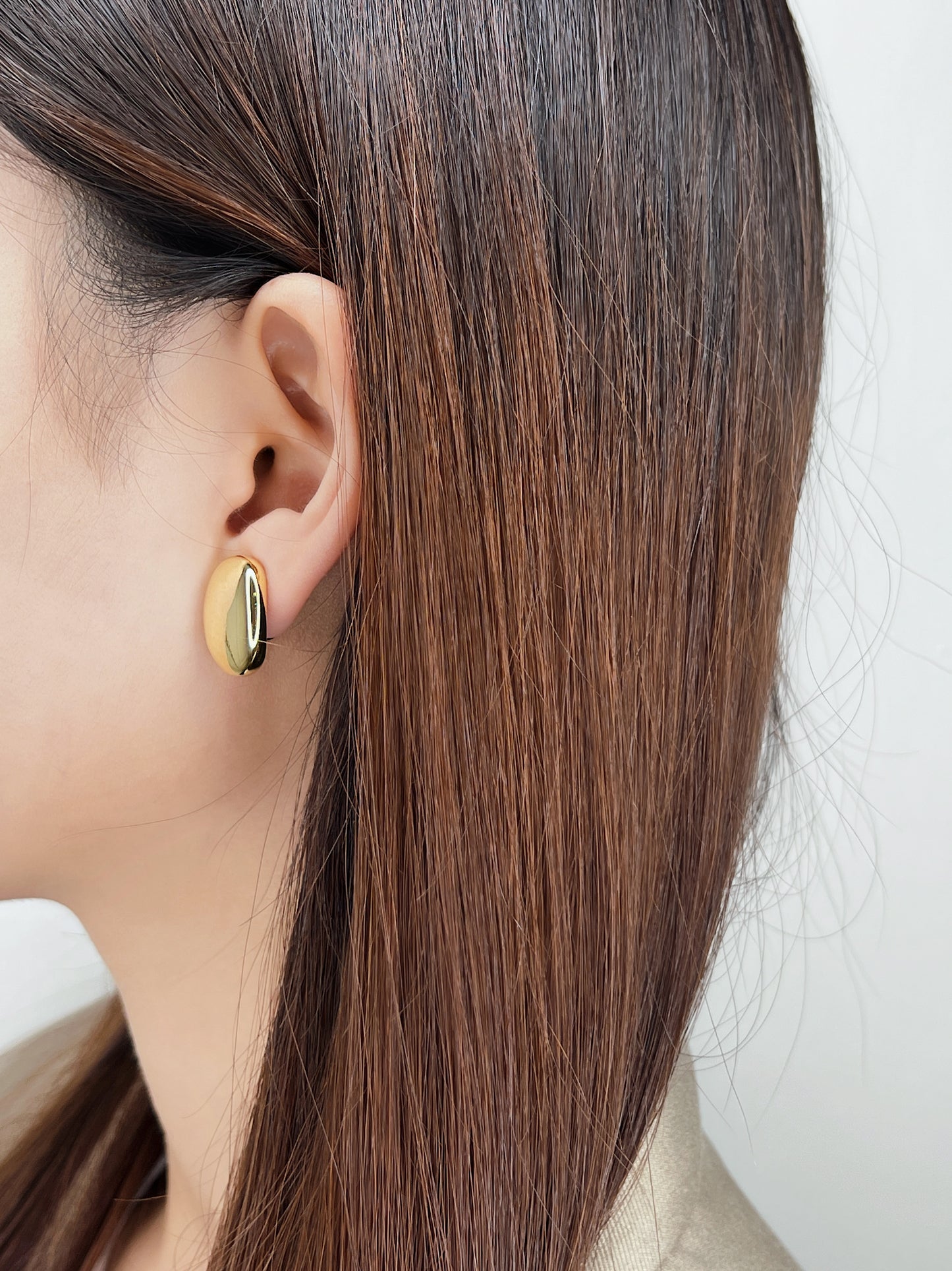 Model with sleek pulled-back hair showcasing the reflective gold finish and subtle side profile of the statement clip earrings.