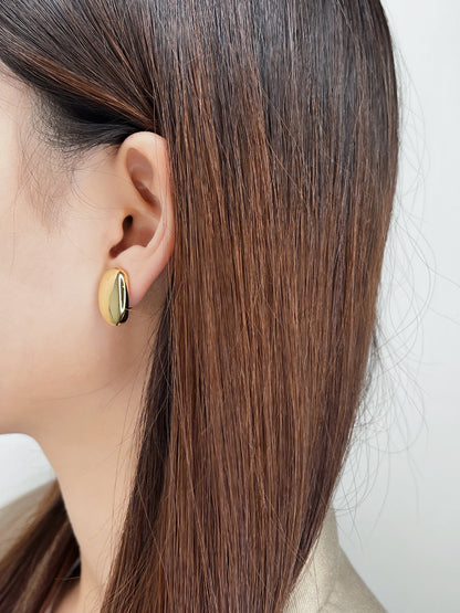 Model with sleek pulled-back hair showcasing the reflective gold finish and subtle side profile of the statement clip earrings.