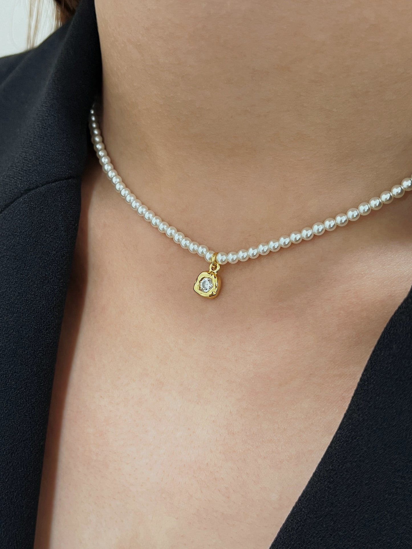 Model profile displaying the Alta pearl necklace contoured high on the throat paired with a sharp black blazer neckline