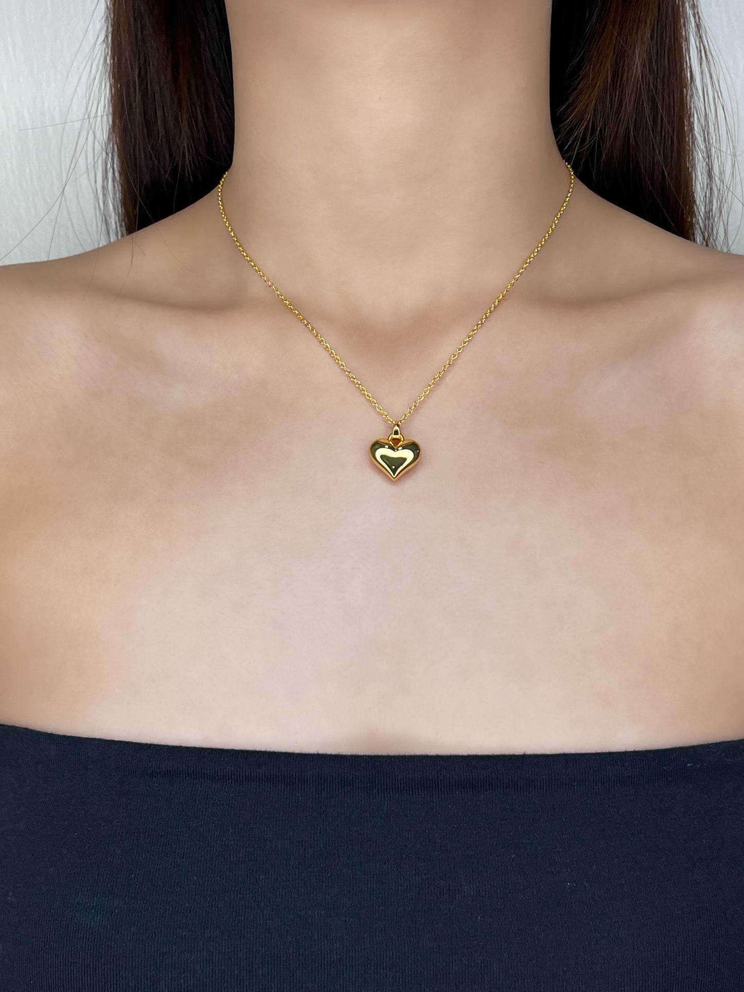 Model profile view displaying the bold gold Lia heart necklace draped elegantly over a clean, modern tube top neckline