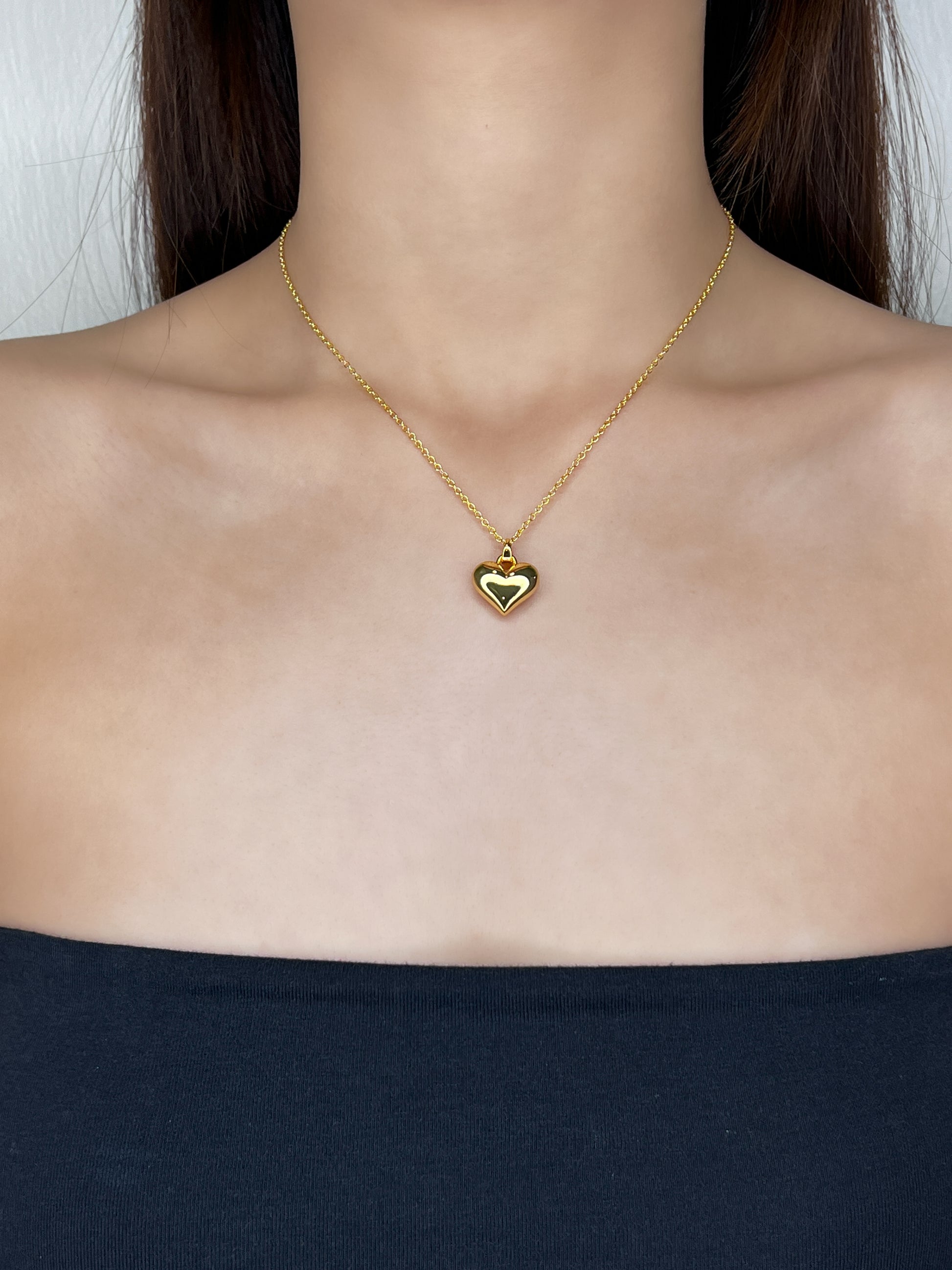Model profile view displaying the bold gold Lia heart necklace draped elegantly over a clean, modern tube top neckline