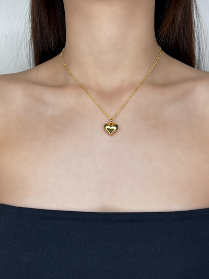 Model profile view displaying the bold gold Lia heart necklace draped elegantly over a clean, modern tube top neckline