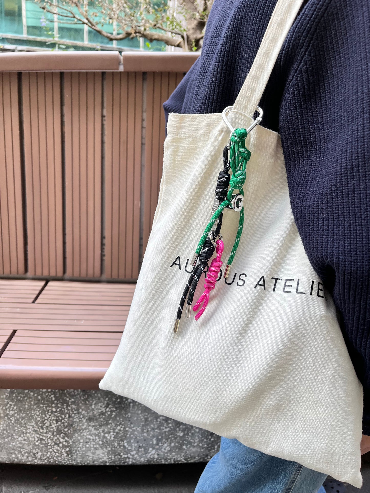 High street commute snapshot showing a canvas tote bag styled with a vibrant green initial charm and black pink personalised charm