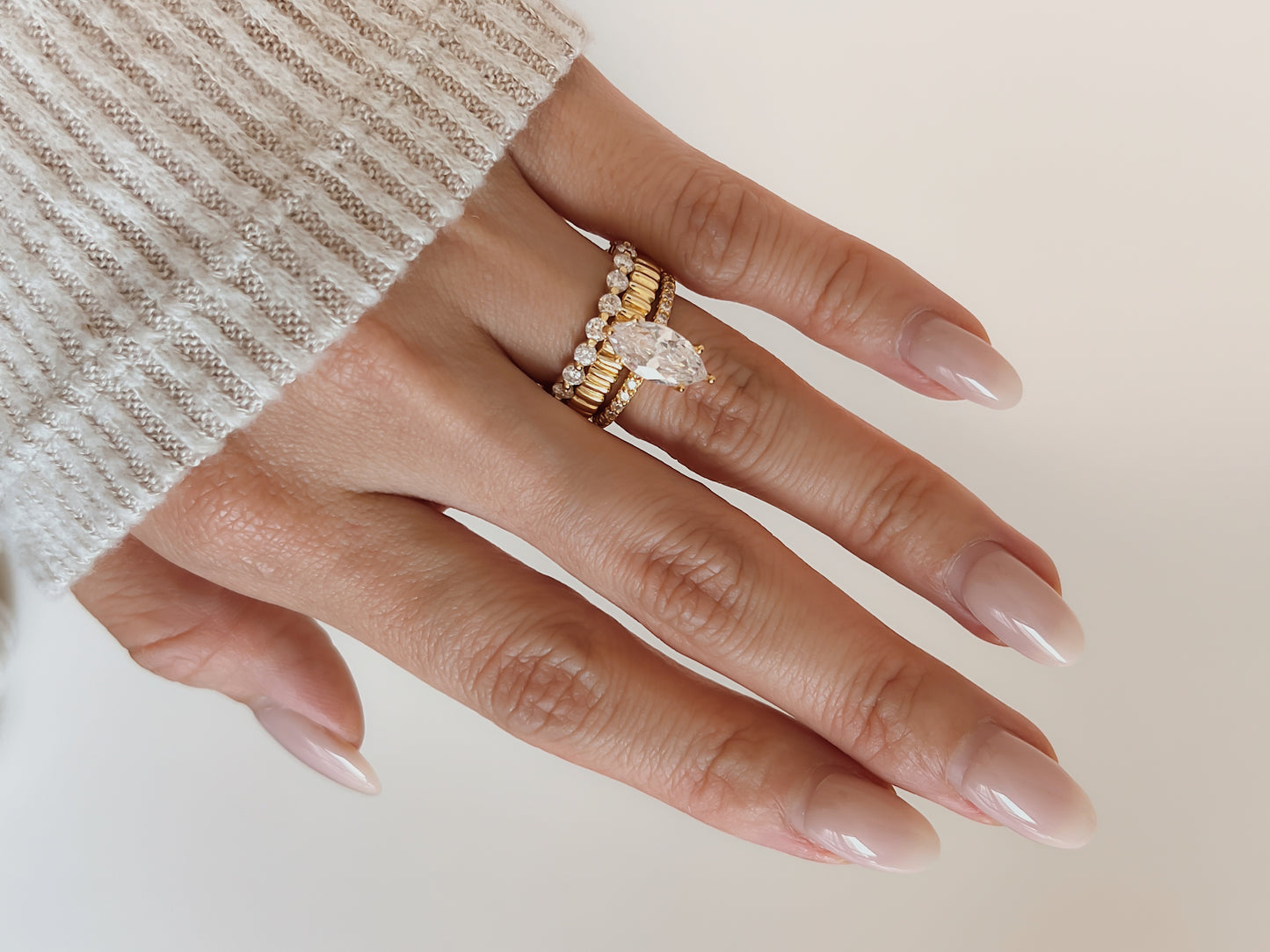 Close up lookbook profile of a model hand wearing the Callie moissanite eternity ring layered inside a heavy gold stack